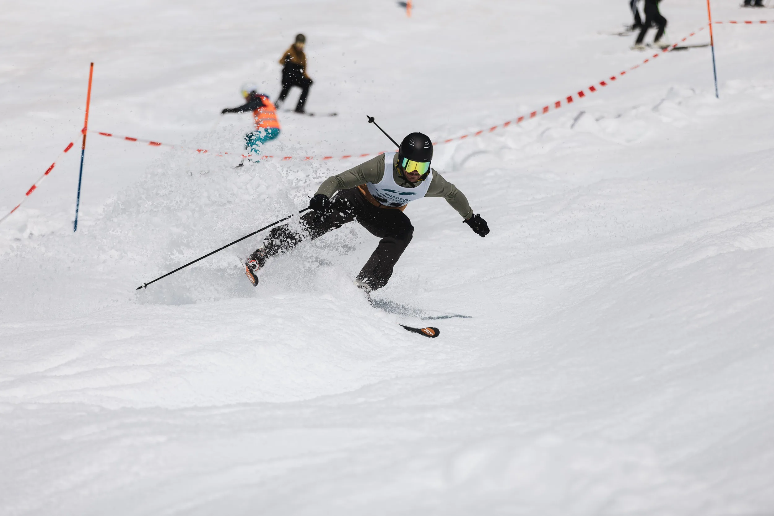 Skifahrer legt sich mit aufstiebendem Schnee in einen Torlauf-Schwung am sonnigen Frühlingshang