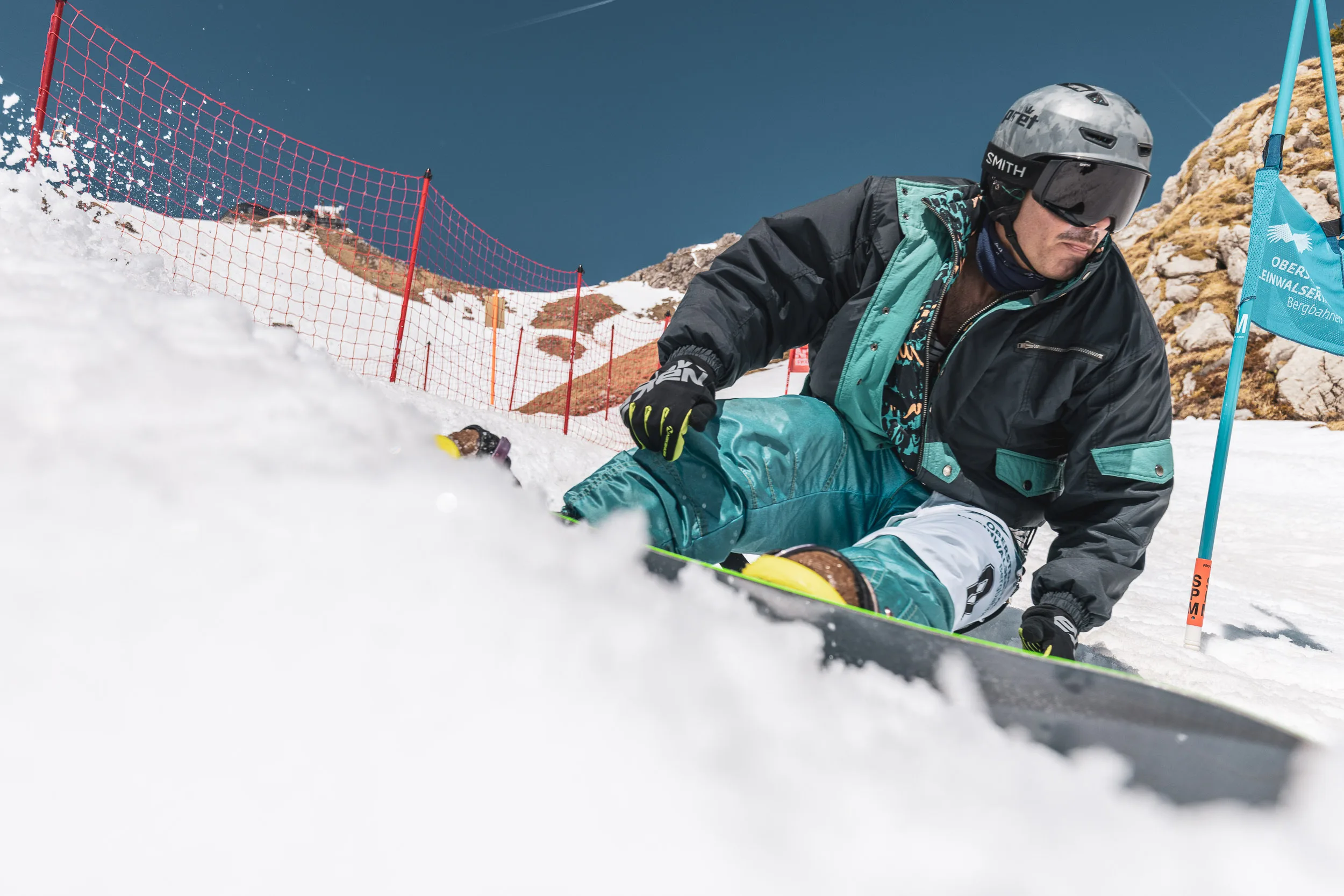 Snowboarder reißt eine große Schneefontäne aus dem Steilhang des Banked-Slalom-Kurses