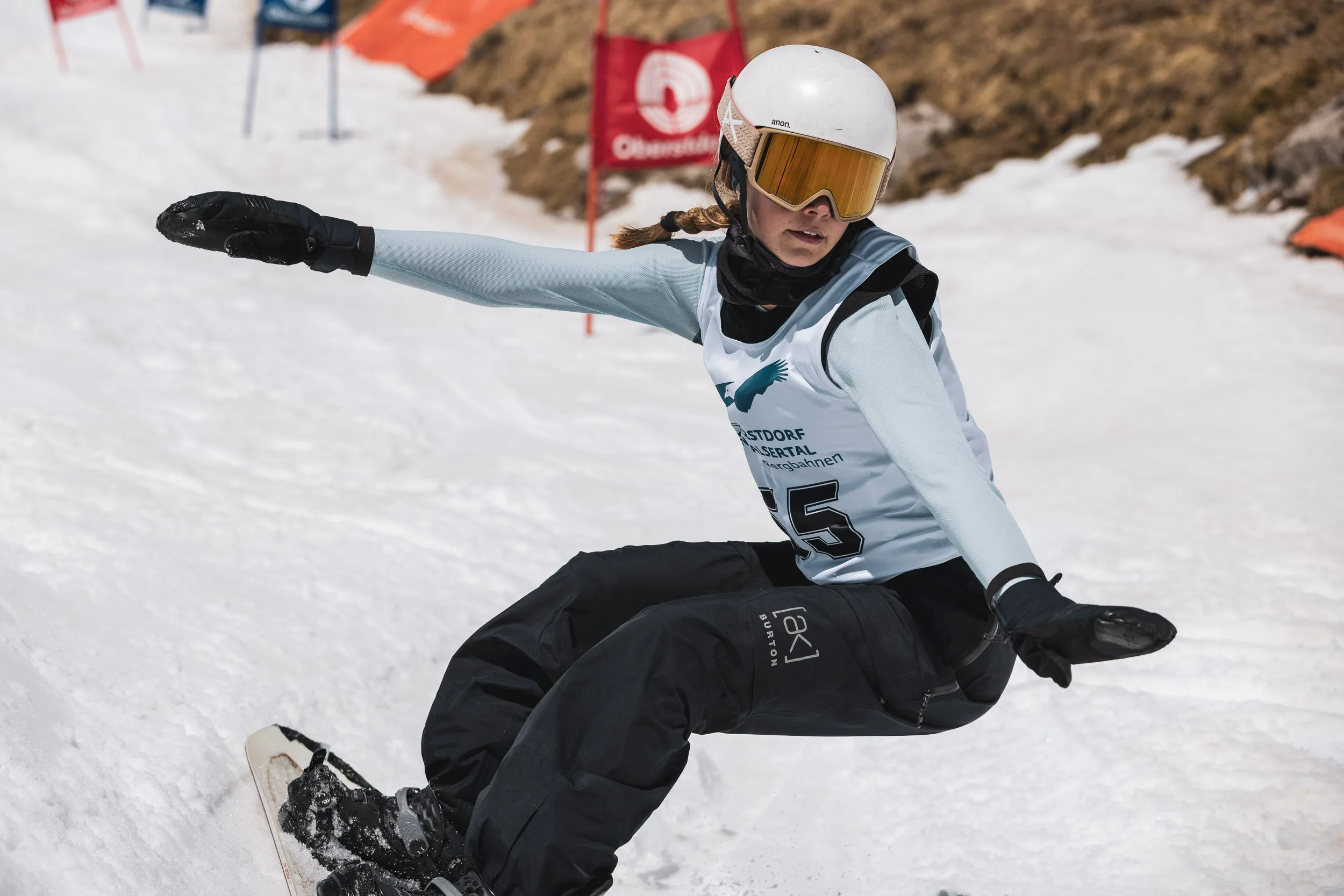 Snowboarder mit Startnummer 5 legt sich tief in einen Carving-Schwung, ausgestreckter Arm über dem Firn