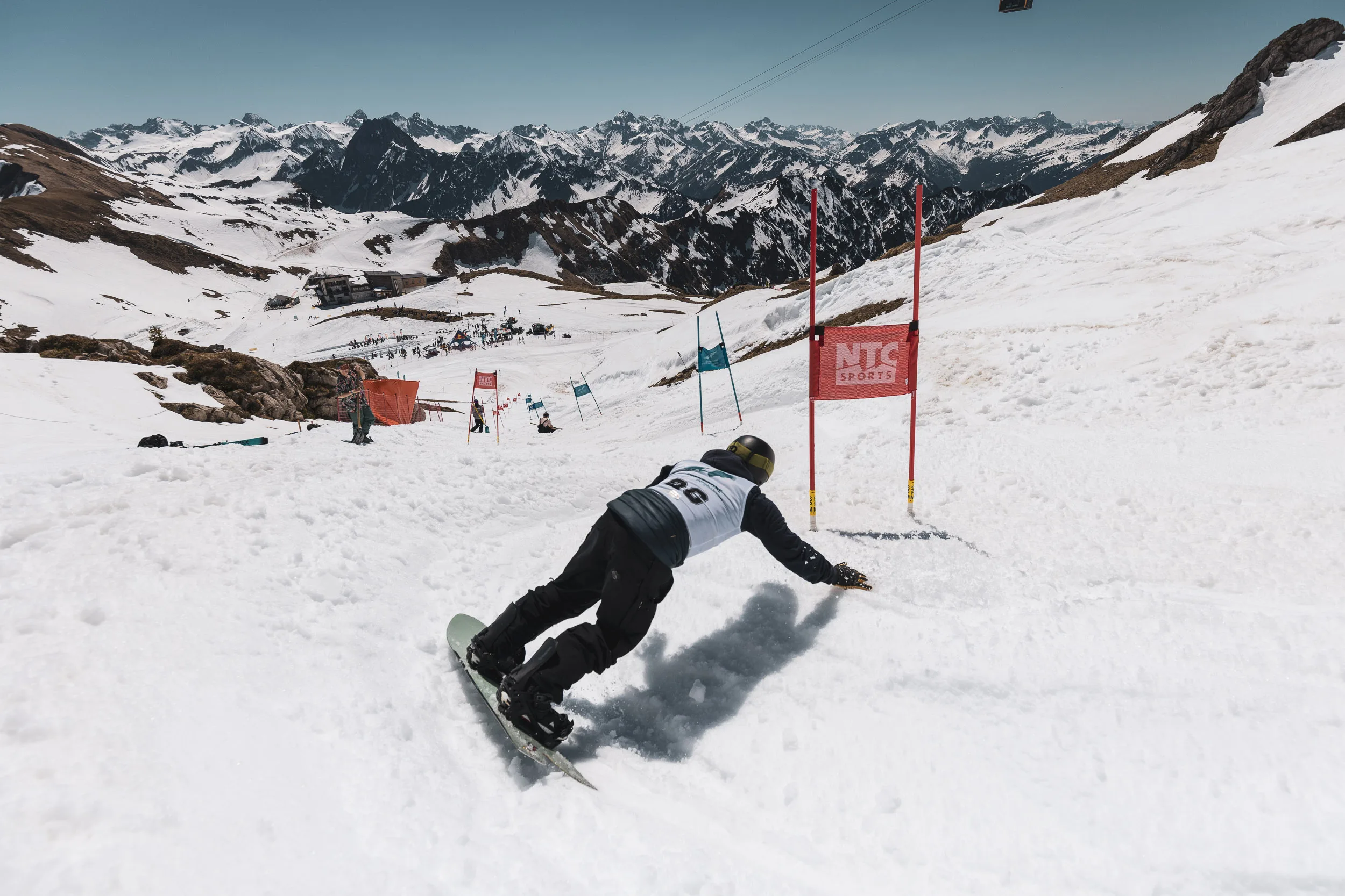 Snowboarder carvt im Banked Slalom über den Frühlingsfirn, dahinter das weite Allgäuer Bergpanorama