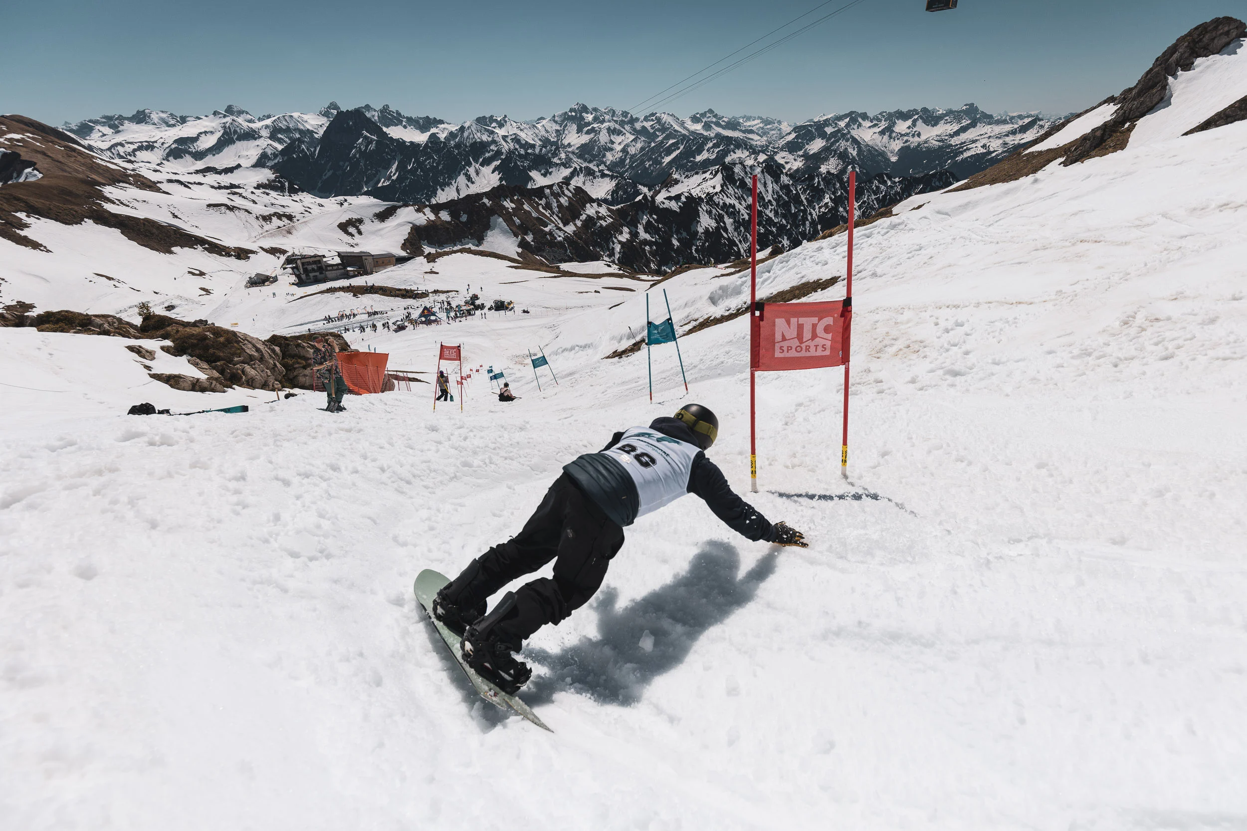 Snowboarder carvt im Banked Slalom über den Frühlingsfirn, dahinter das weite Allgäuer Bergpanorama