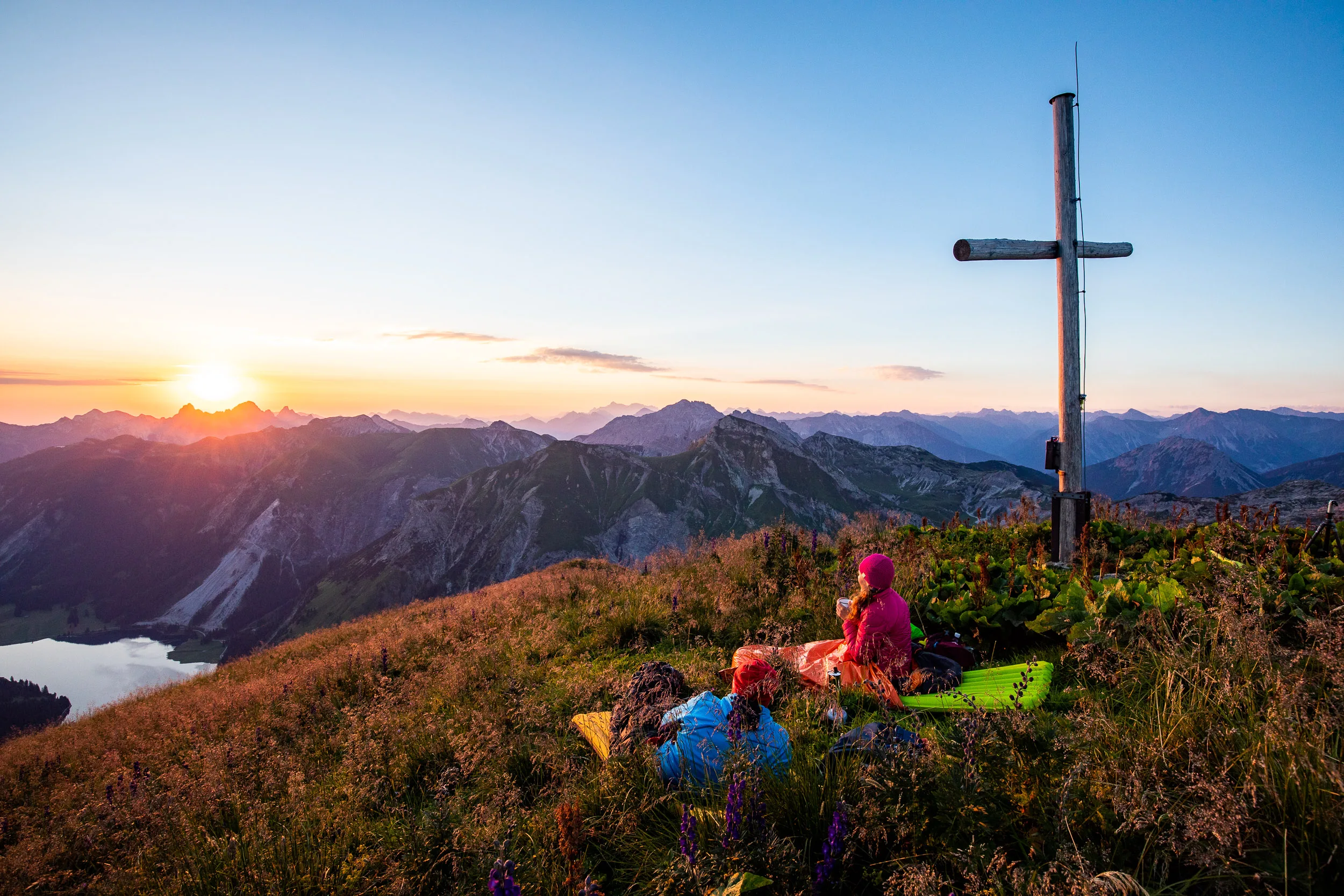Caroline Nantke und Harald Dreyer liegen am Gipfelkreuz auf Matten vor der Abendsonne