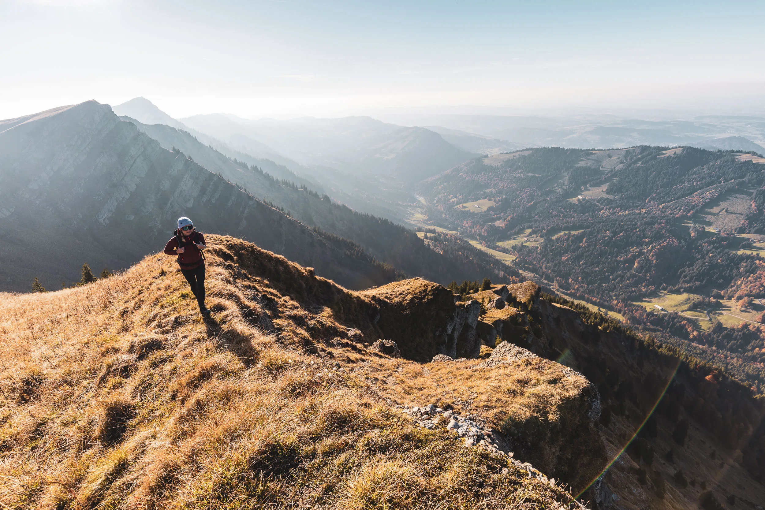 Wanderin geht über einen schmalen grasigen Grat mit weitem Blick ins Tal