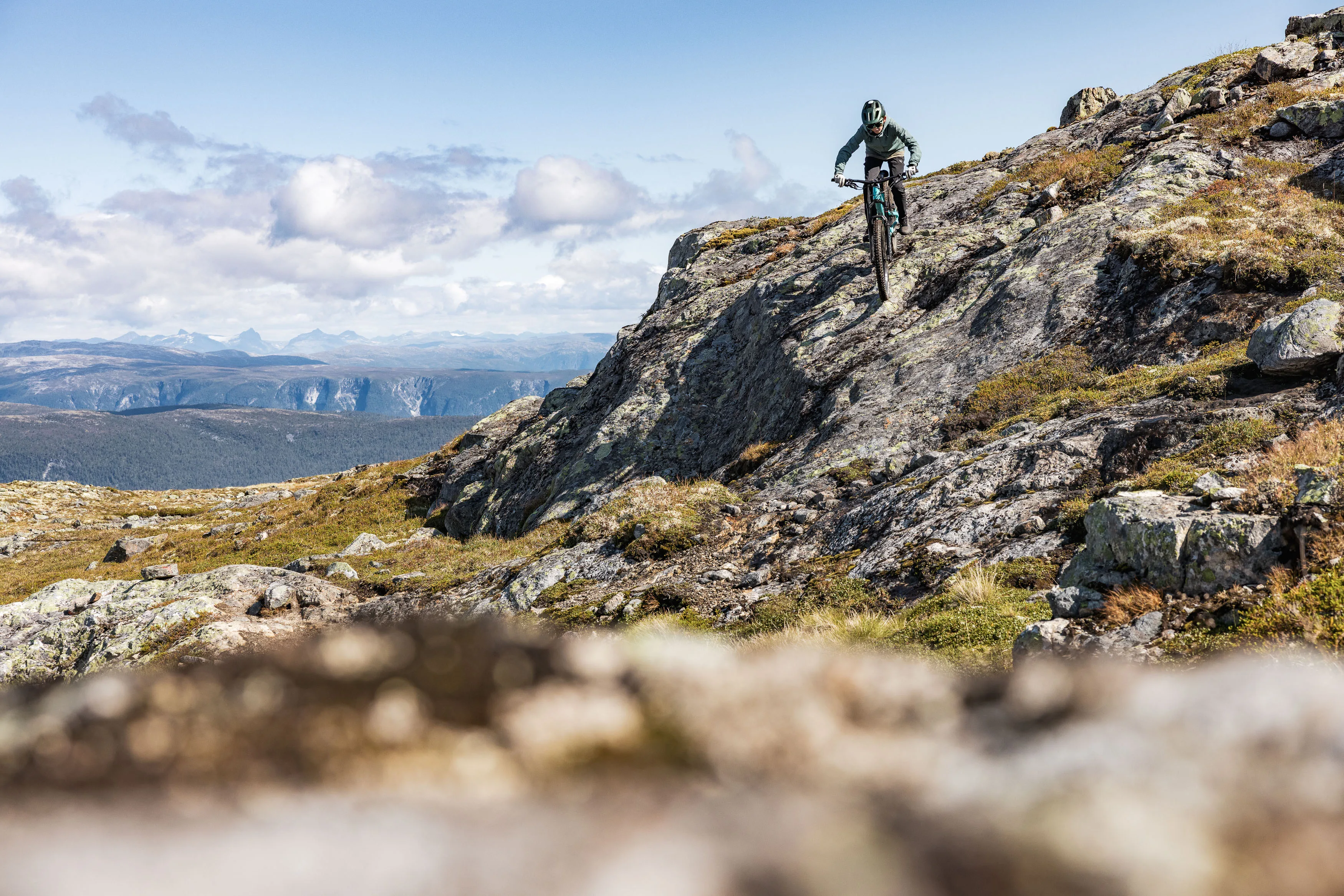 Mountainbiker hält auf einer steilen Felslinie über einer weiten Berglandschaft die Spur