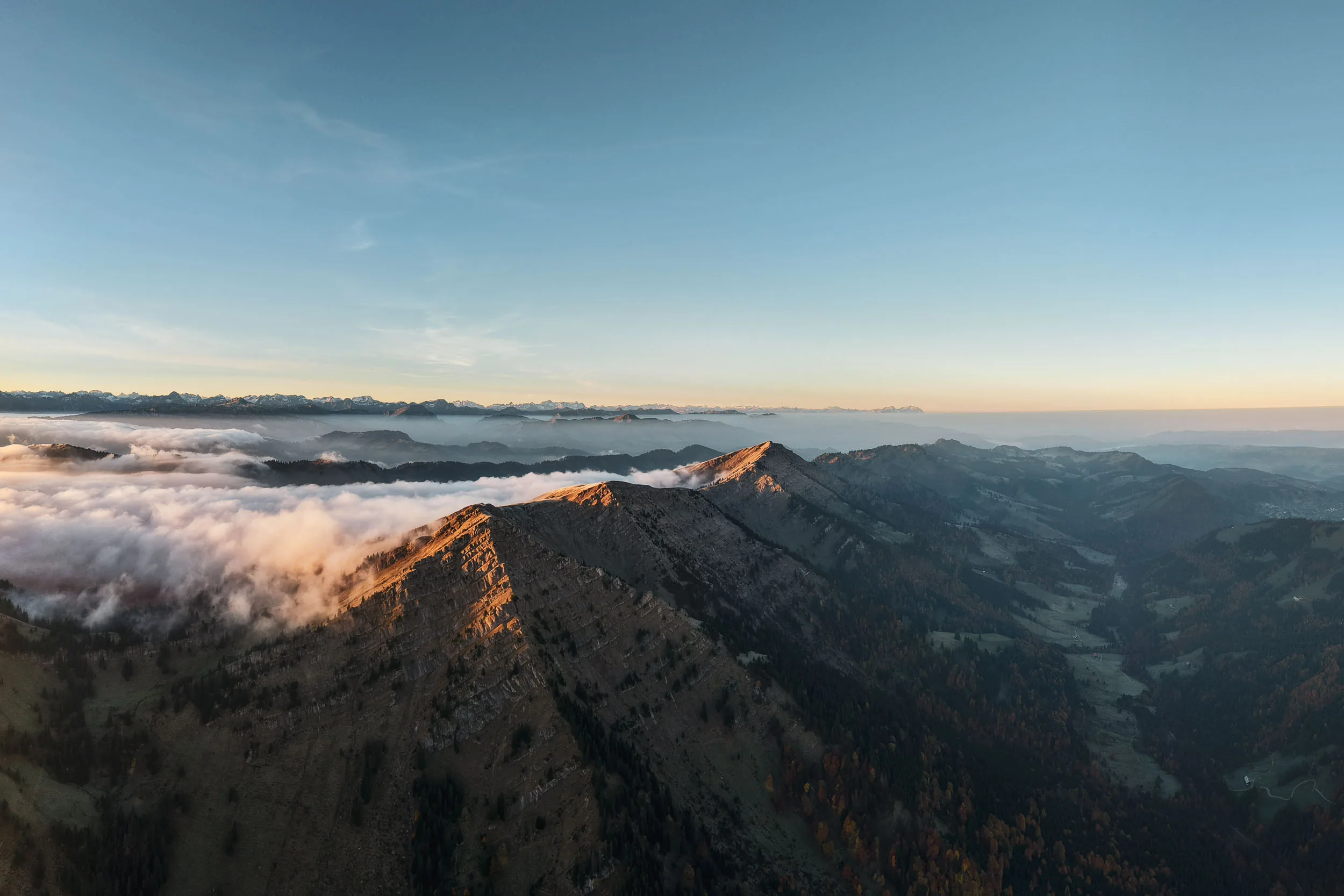 Warmes Morgenlicht trifft einen bewaldeten Bergkamm über tief liegenden Wolken