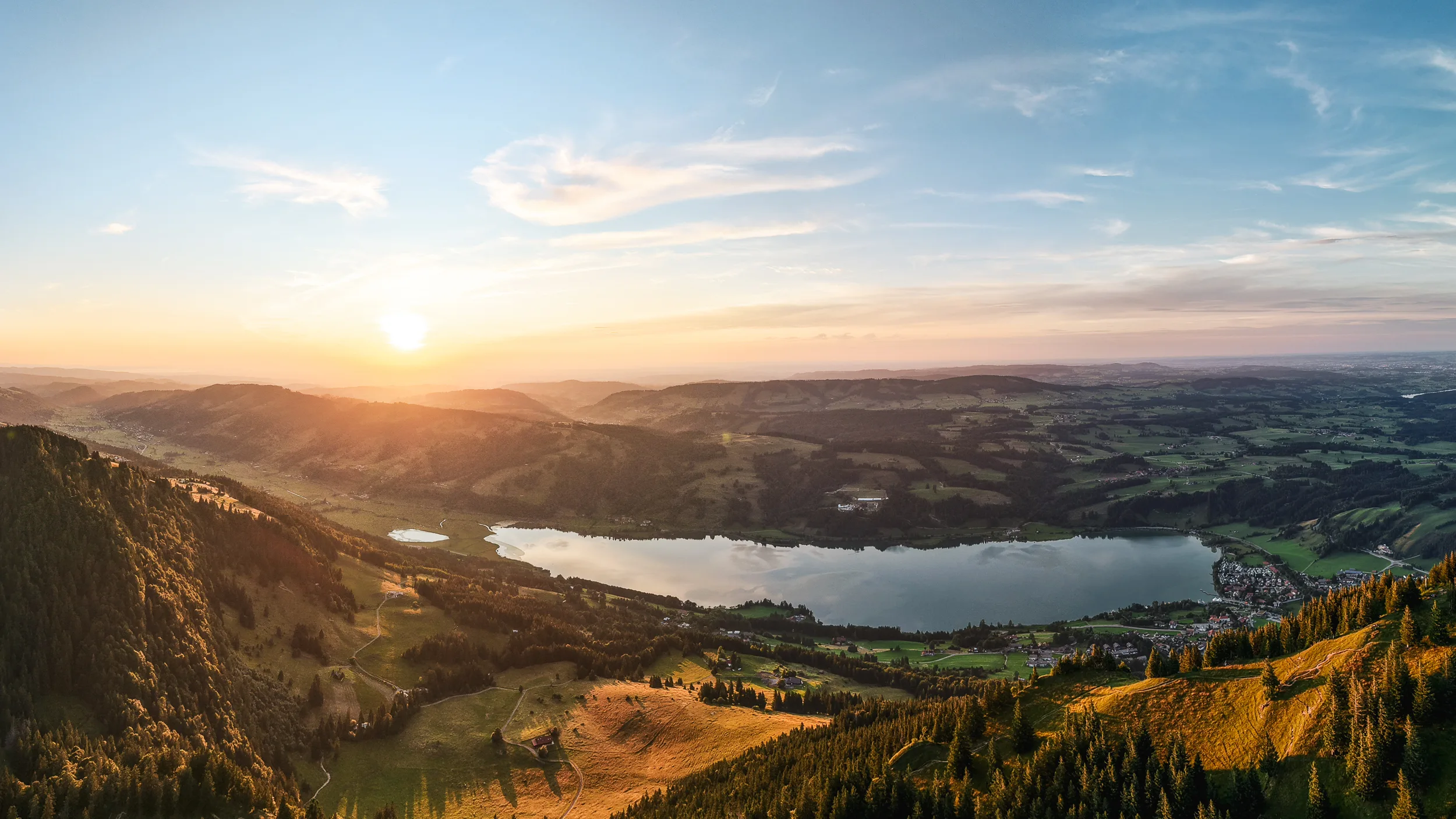 Die Sonne sinkt über dem Großen Alpsee und den bewaldeten Höhen des Allgäus