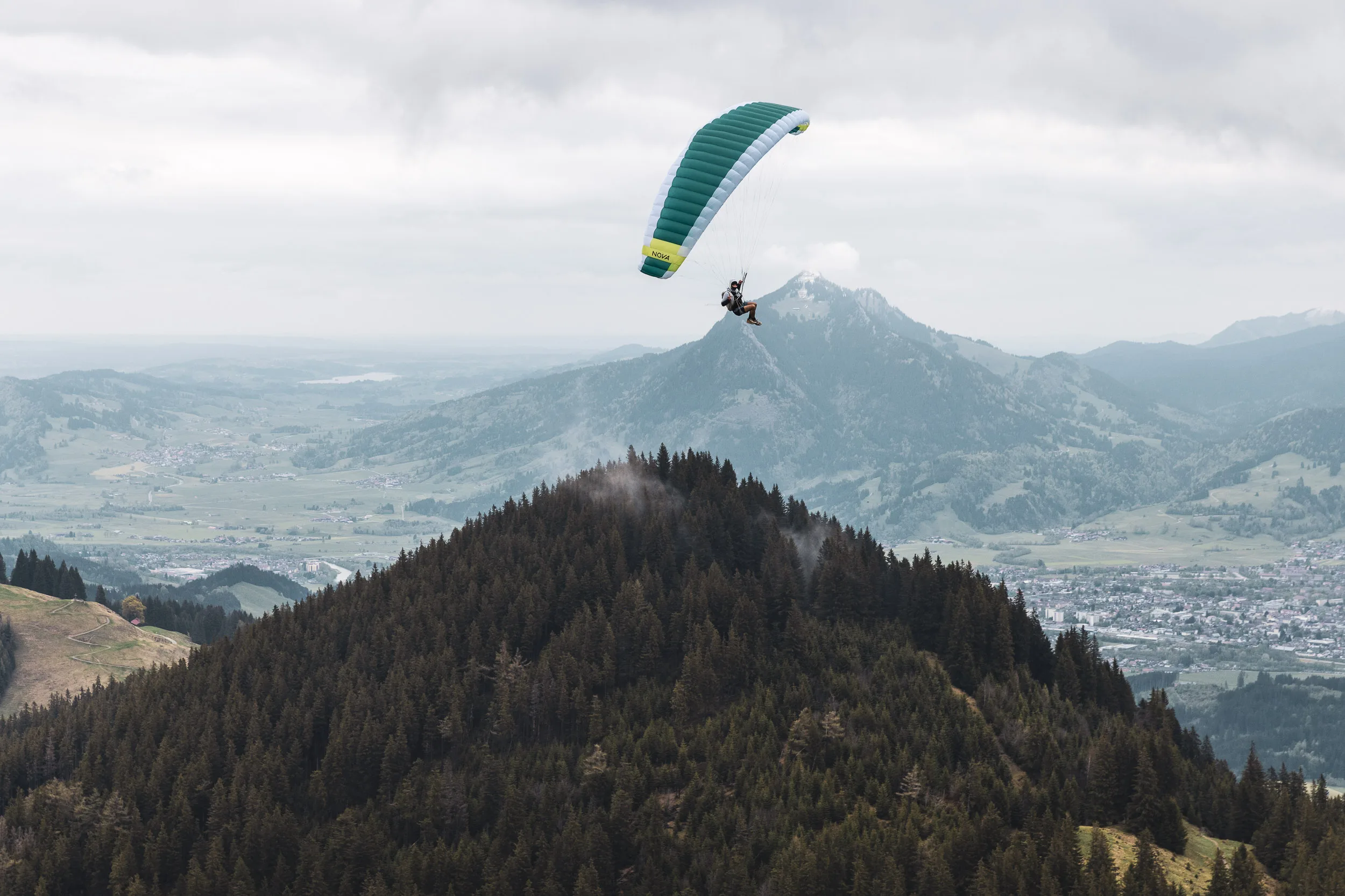 Michael Lacher gleitet mit dem Gleitschirm über bewaldeten Hängen im Allgäu