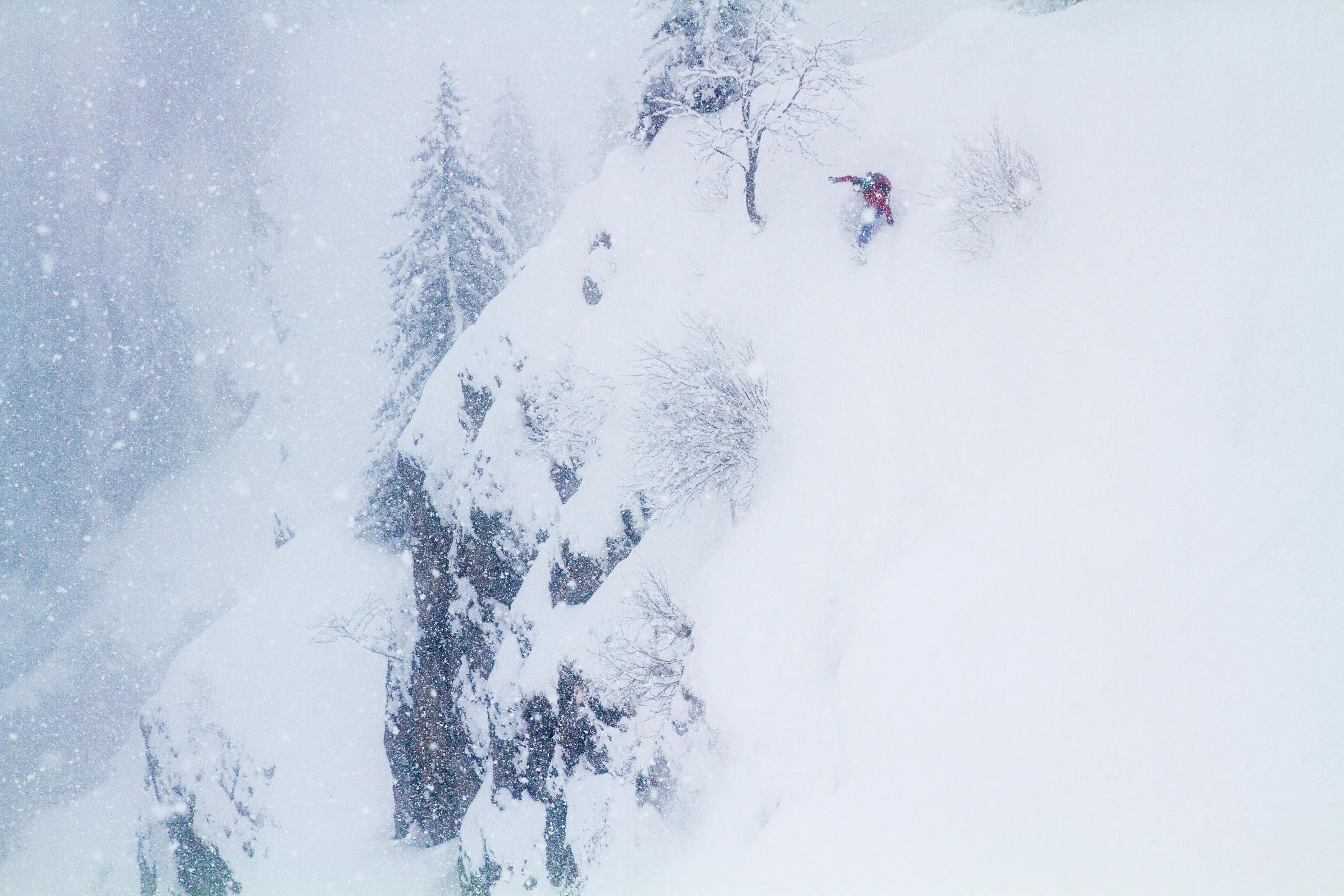 Snowboard fährt durch tiefen Schnee neben einer schneebedeckten Felswand