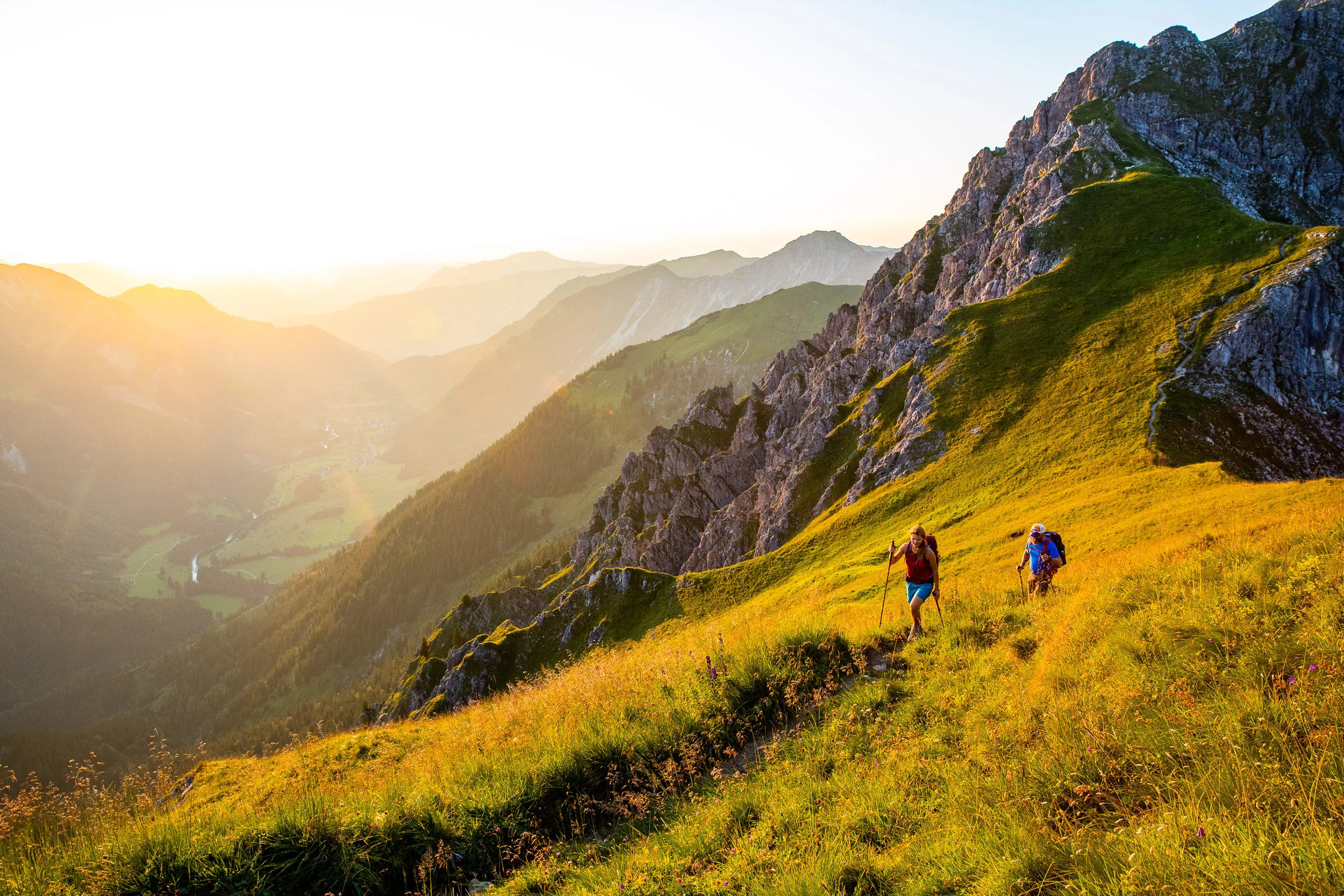 Caroline Nantke und Harald Dreyer wandern über einen leuchtenden Grasgrat unter einem Felsgipfel