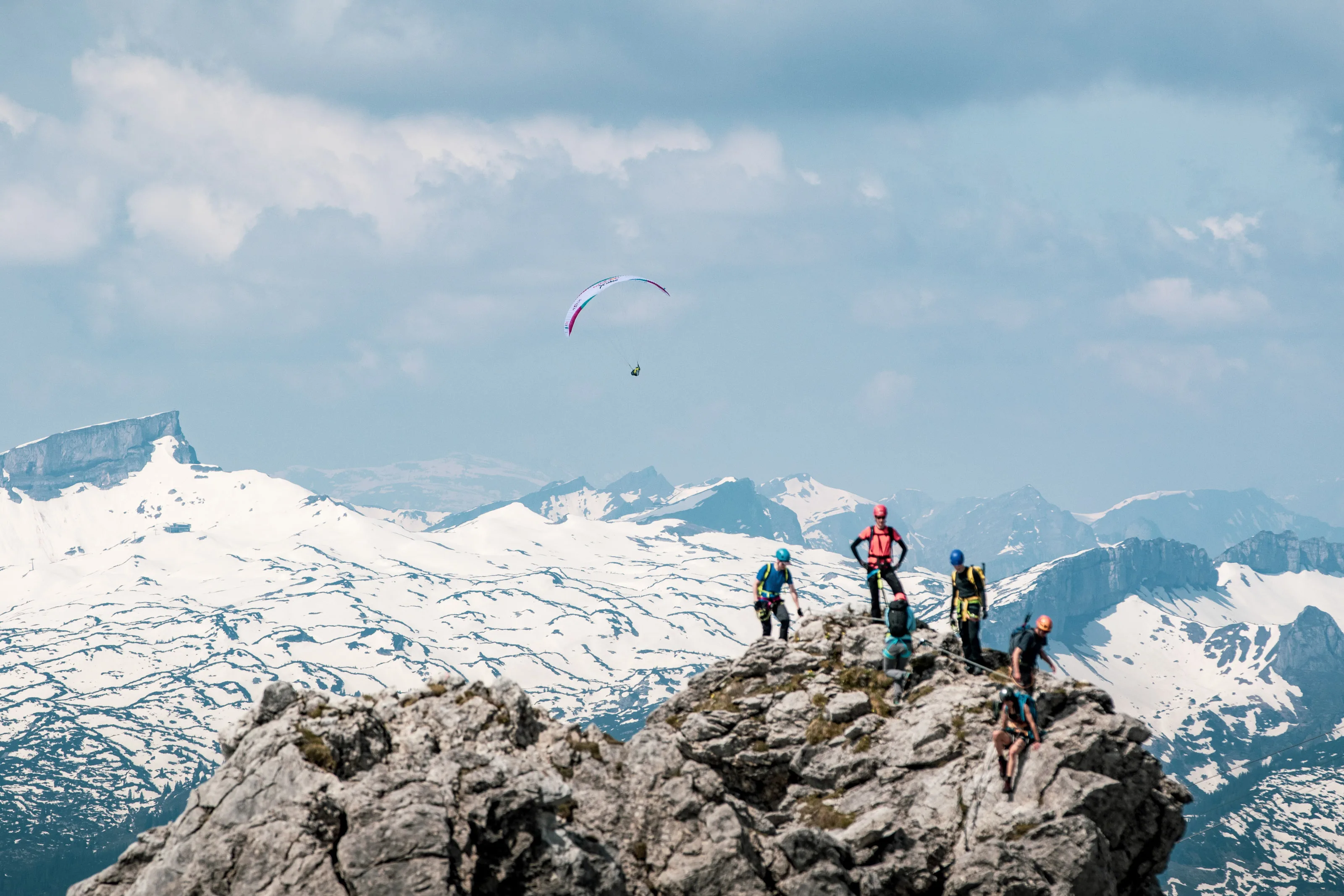 Mehrere Menschen stehen auf einem felsigen Gipfel; dahinter erstreckt sich ein weites Schneepanorama.
