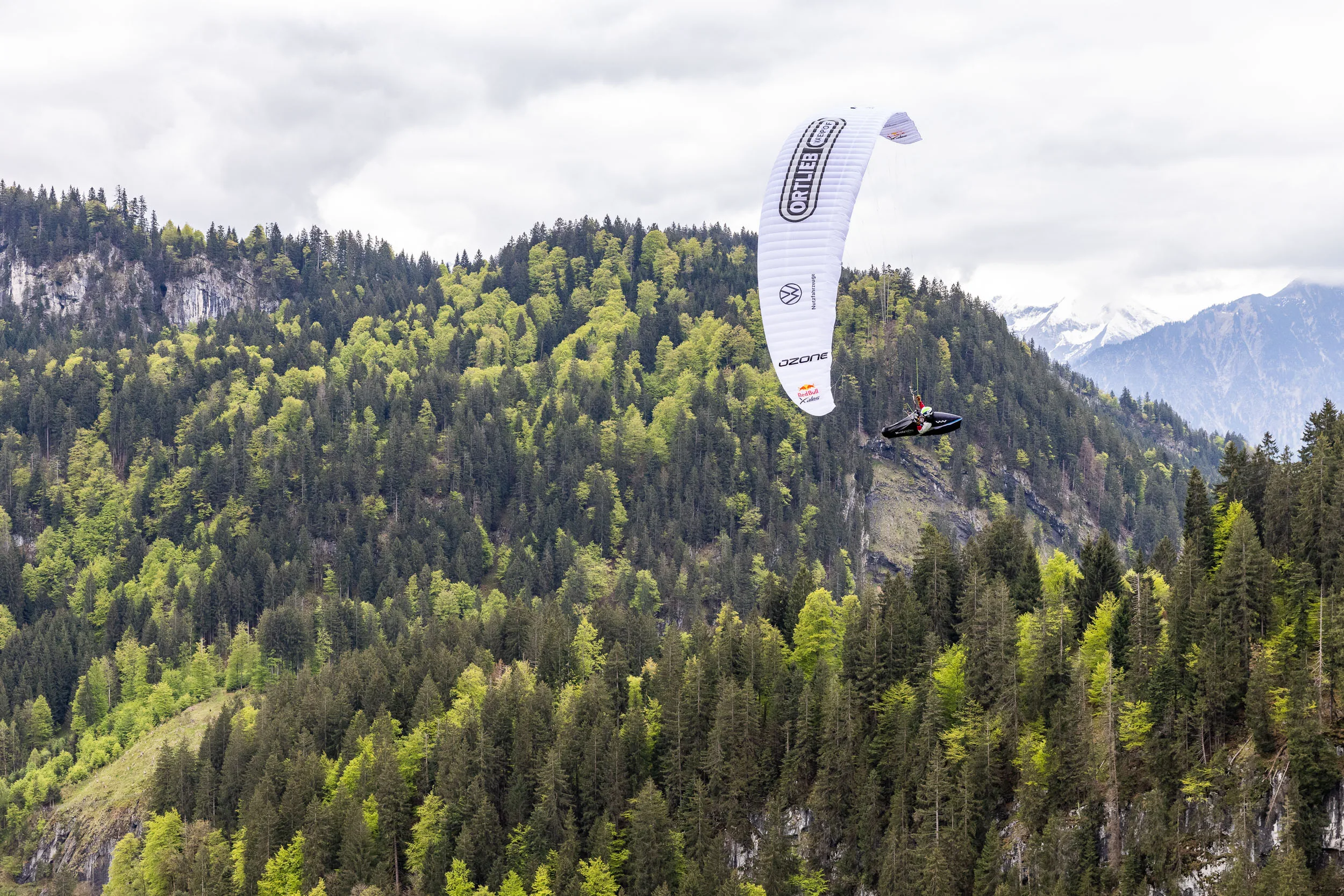 Eli Egger fliegt mit Gleitschirm vor einem bewaldeten Berghang im Allgaeu.