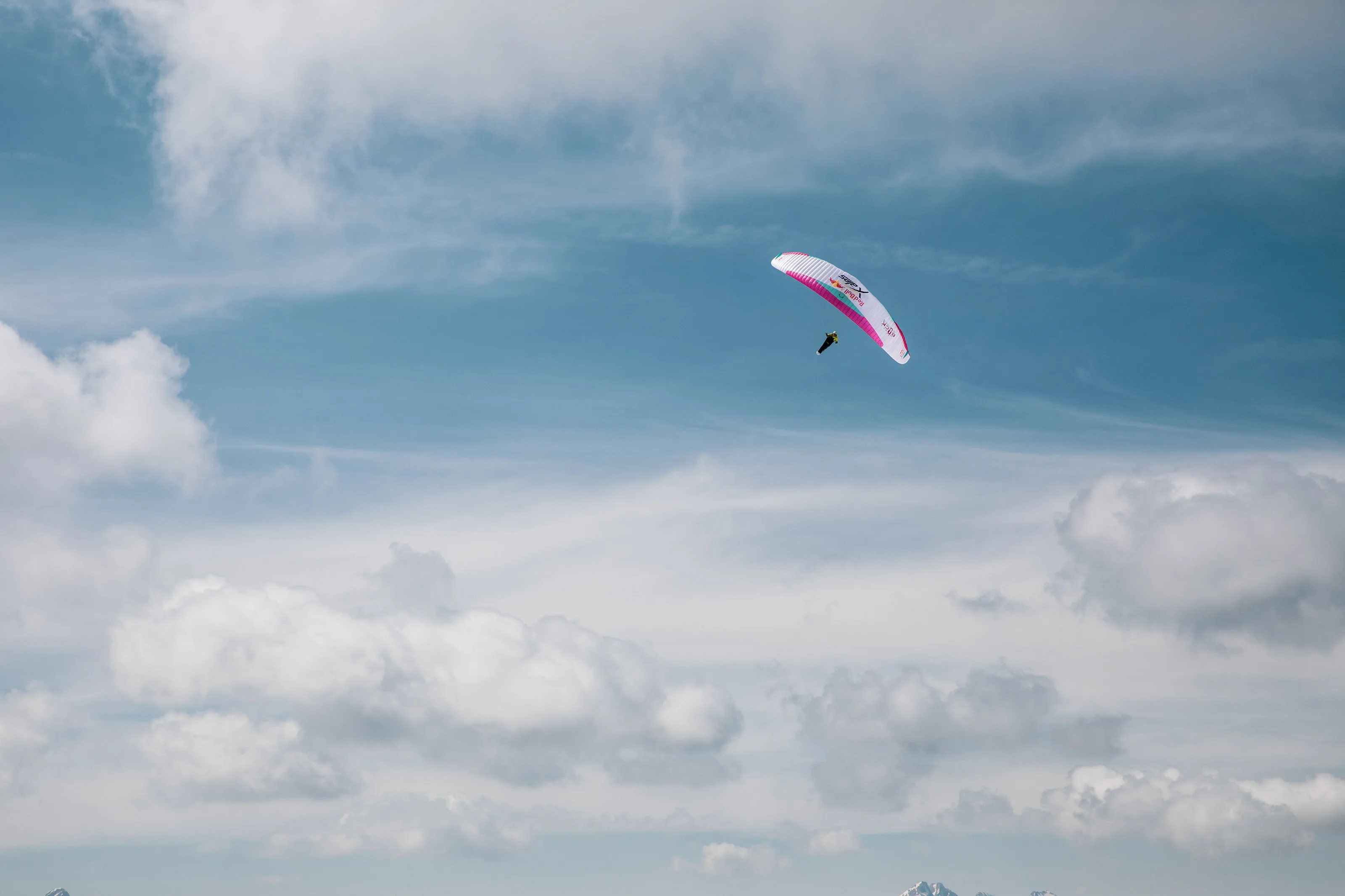 Michael Lacher fliegt mit dem Gleitschirm vor gestaffelten Wolken über dem Bergpanorama.