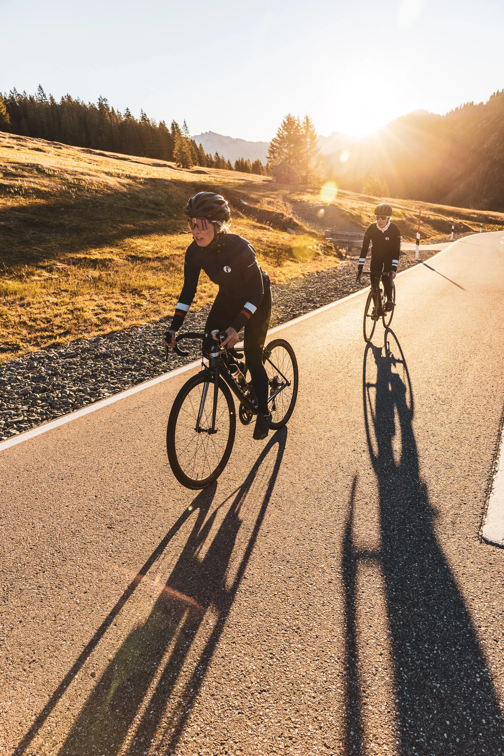 Zwei Rennradfahrerinnen fahren mit langen Schatten über den Asphalt
