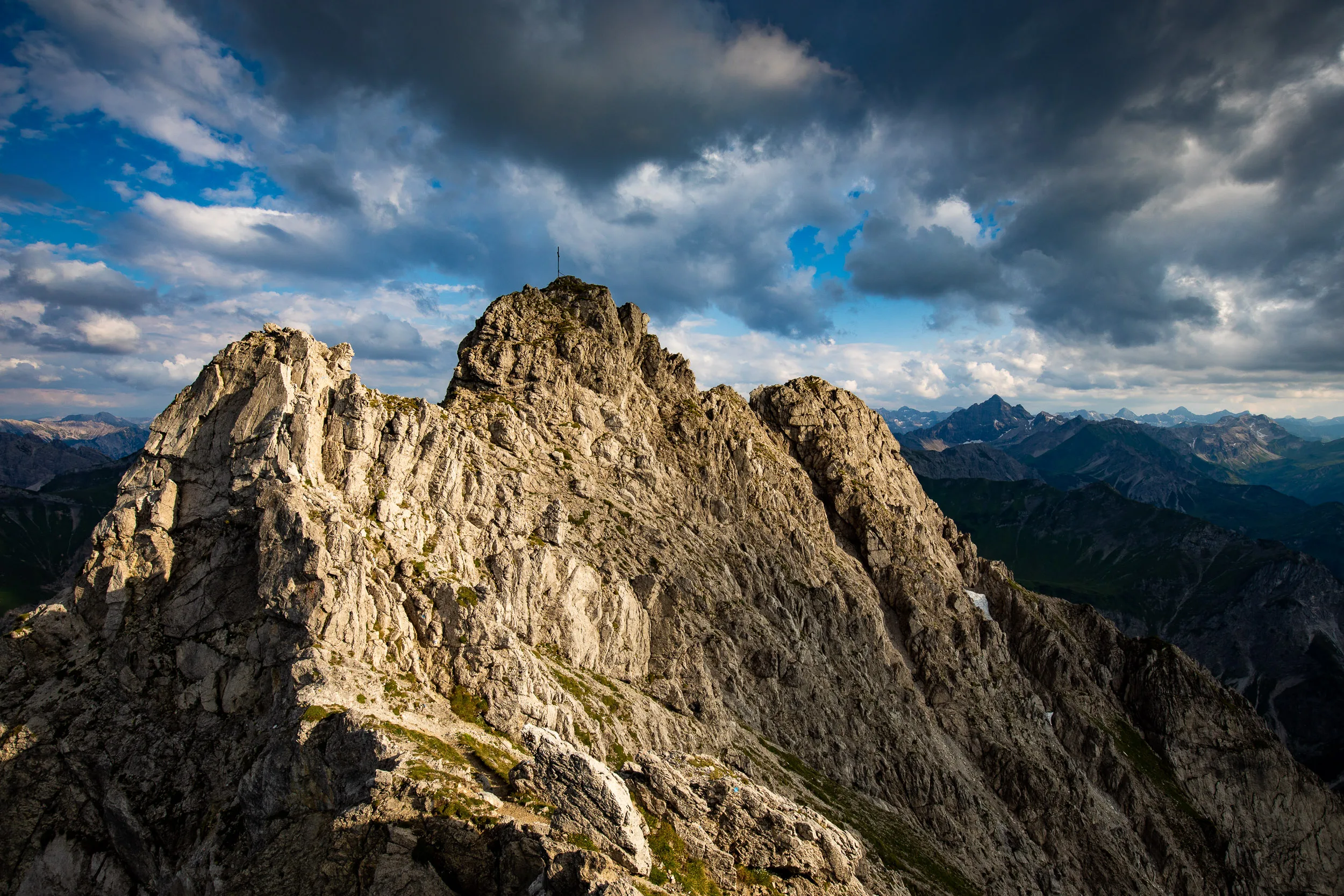 Ein zerklüfteter Felsgrat liegt im warmen Licht vor dunklen Wolken