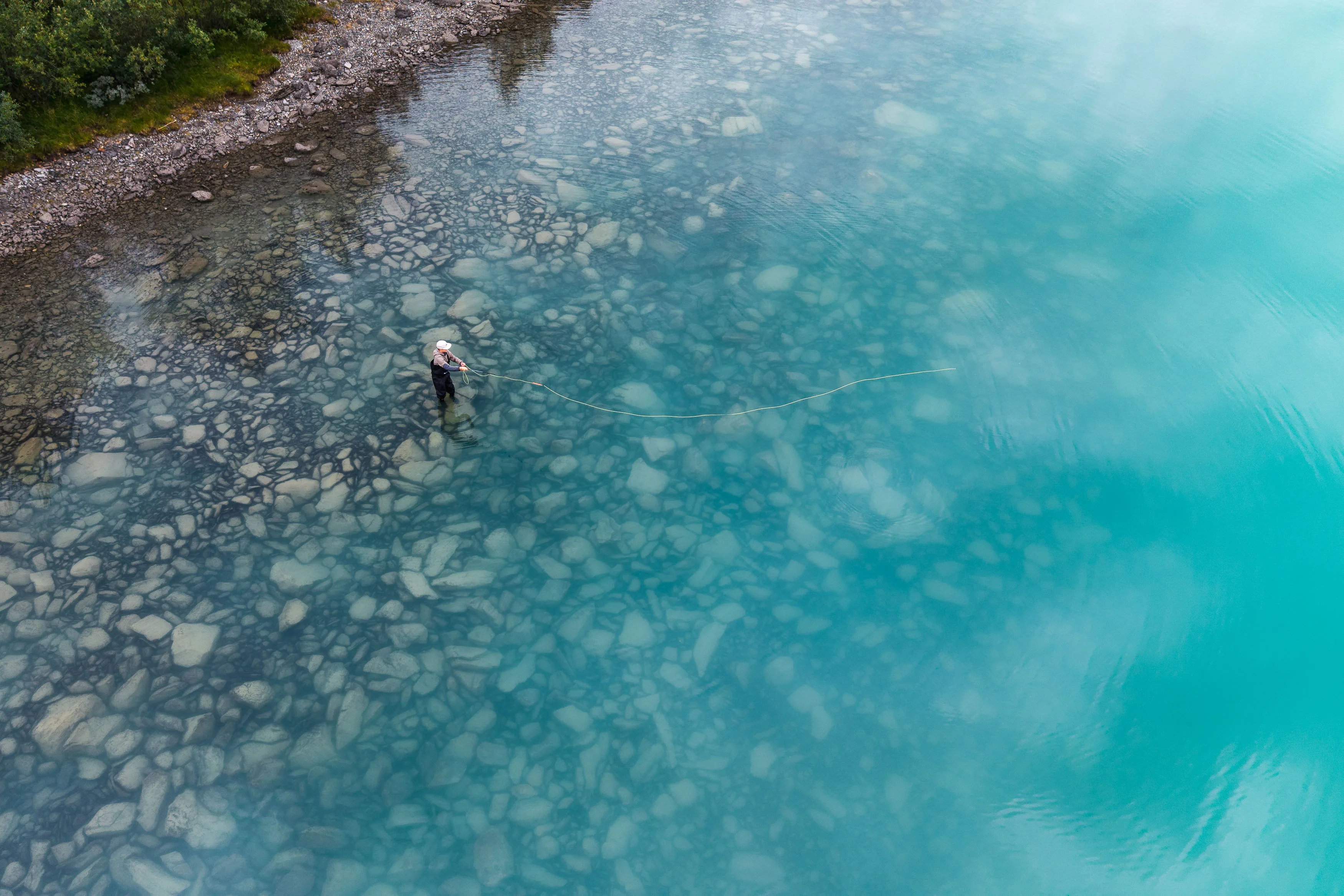 Luftaufnahme eines Anglers zwischen hellem Kiesbett und tiefblauem Wasser