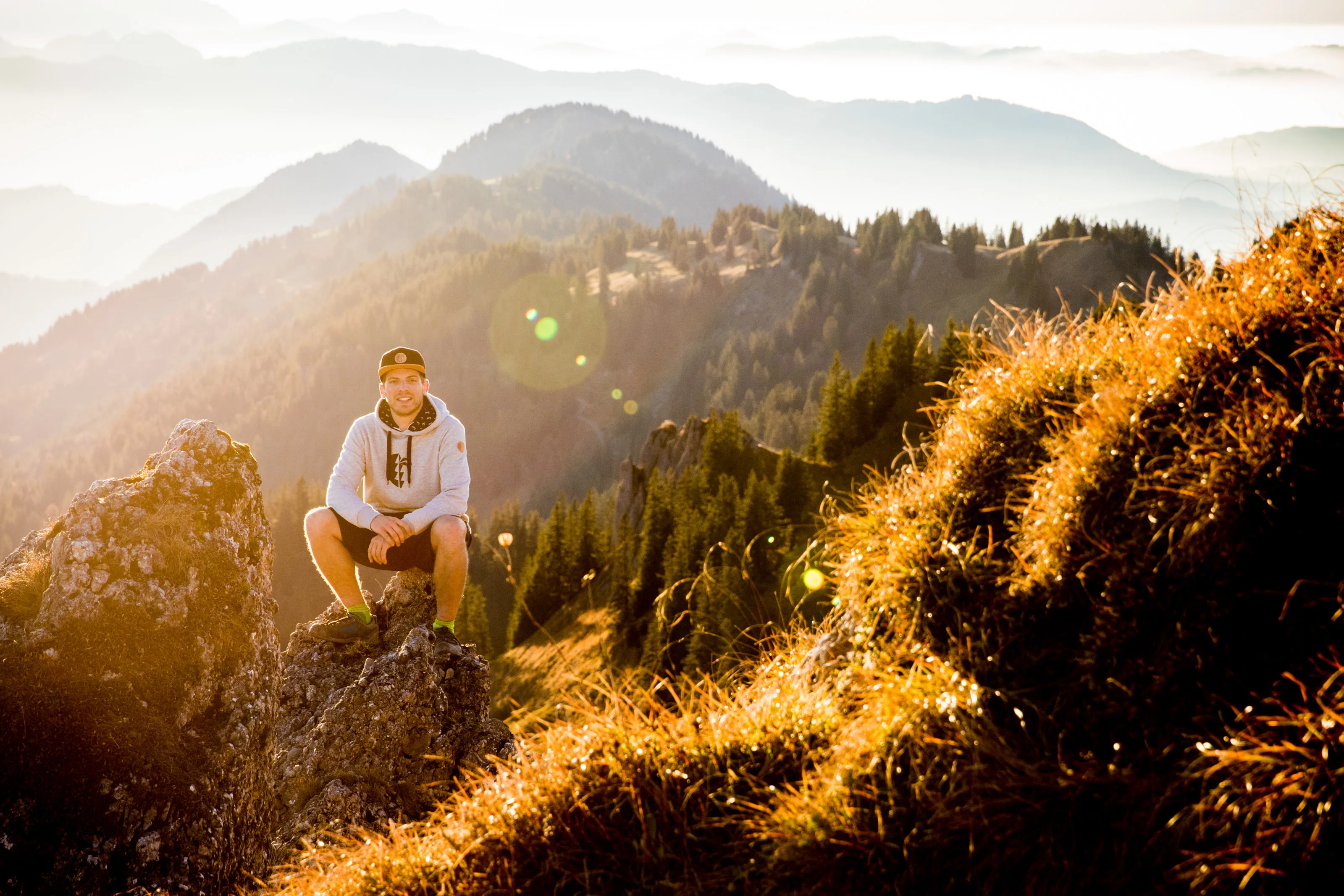 Florian Häusler sitzt auf einem Felsen vor bewaldeten Bergen.