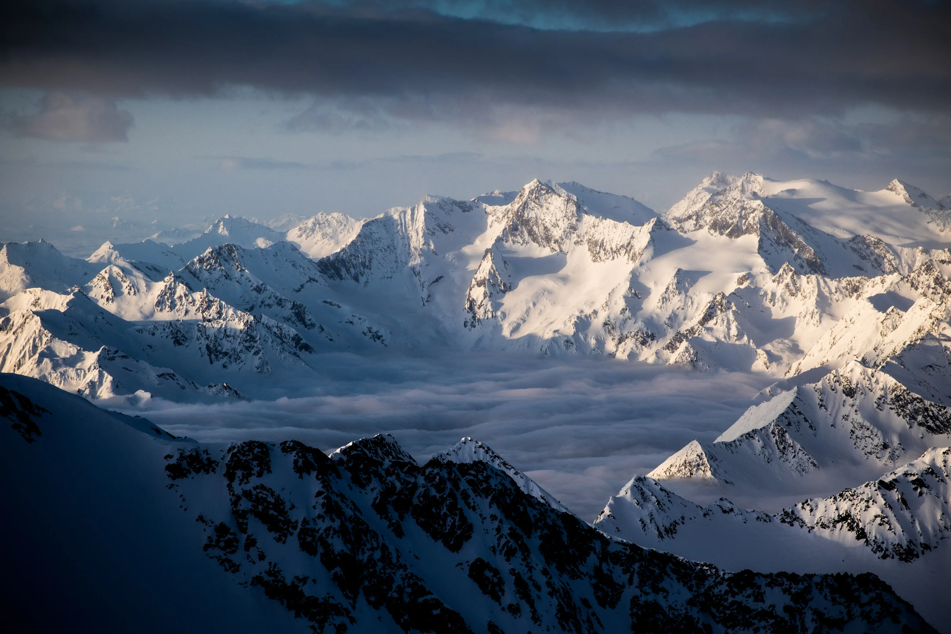 Schneebedeckte Gipfelkette im tiefen Winterlicht über den Wolken in Tirol