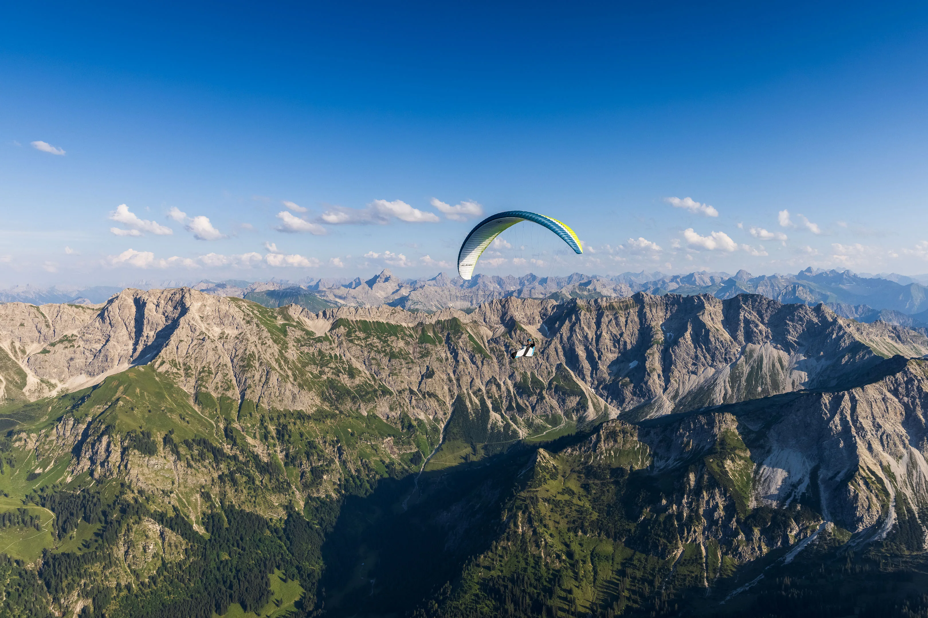 Ein Gleitschirm schwebt über einem schattigen Kar zwischen sonnigen Bergkämmen