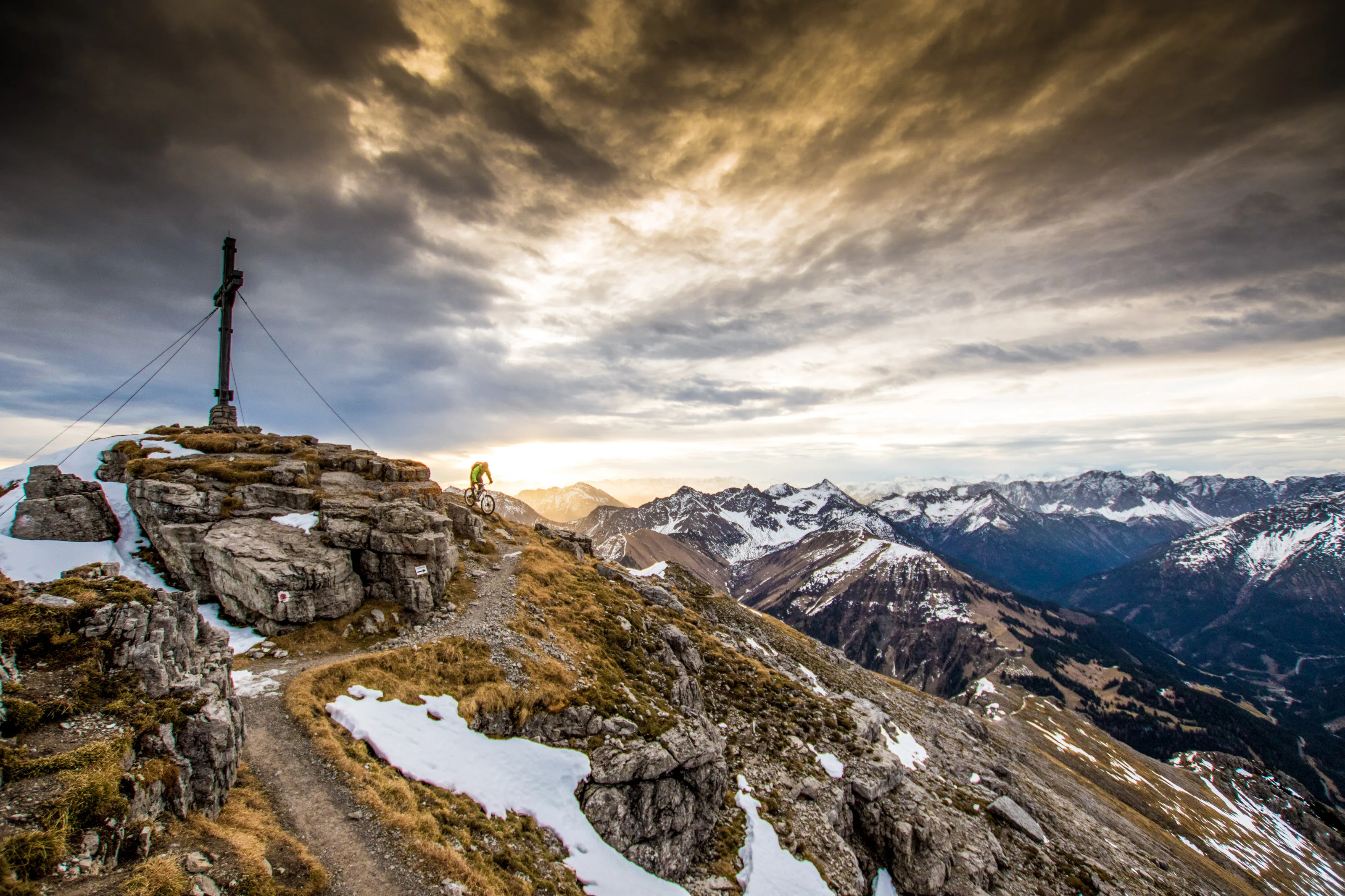 Florian Bergmann fährt mit dem Mountainbike unter einem Gipfelkreuz am Thaneller in Tirol.