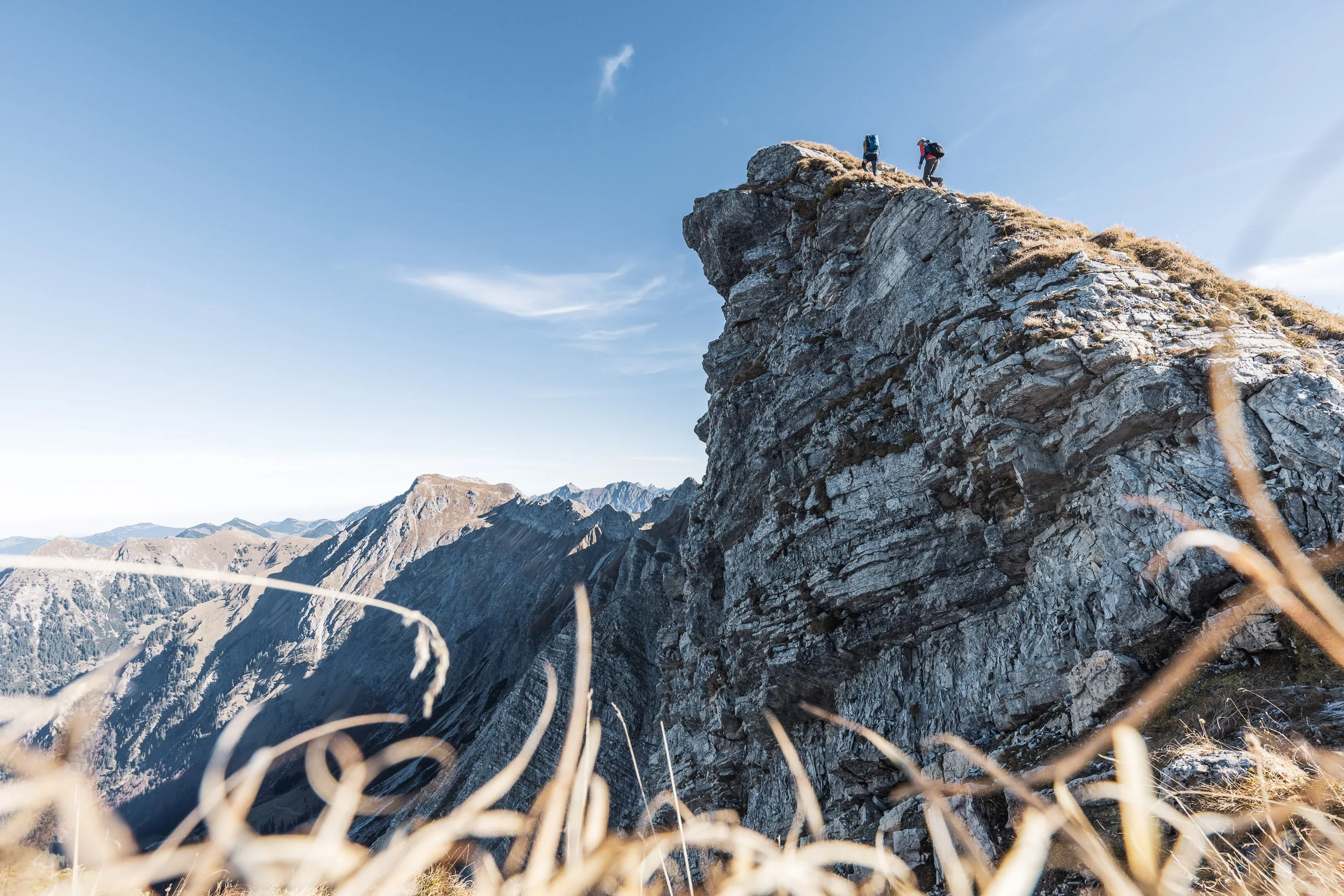 Zwei Bergsteiger bewegen sich auf einem schmalen Grat über einer steilen Felswand.