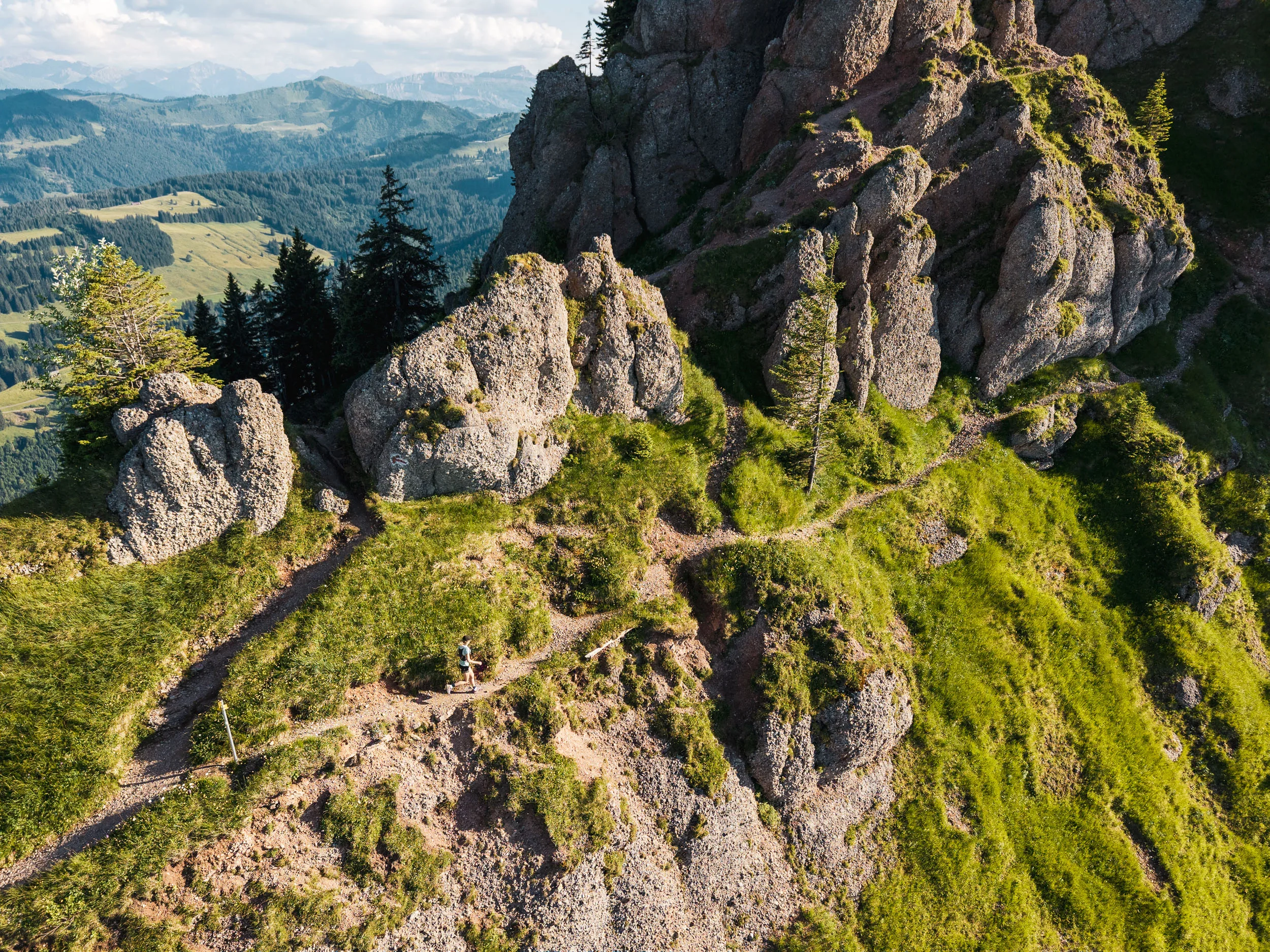 Eine Trailrunnerin quert einen schmalen Pfad unter markanten Felstürmen der Nagelfluhkette.