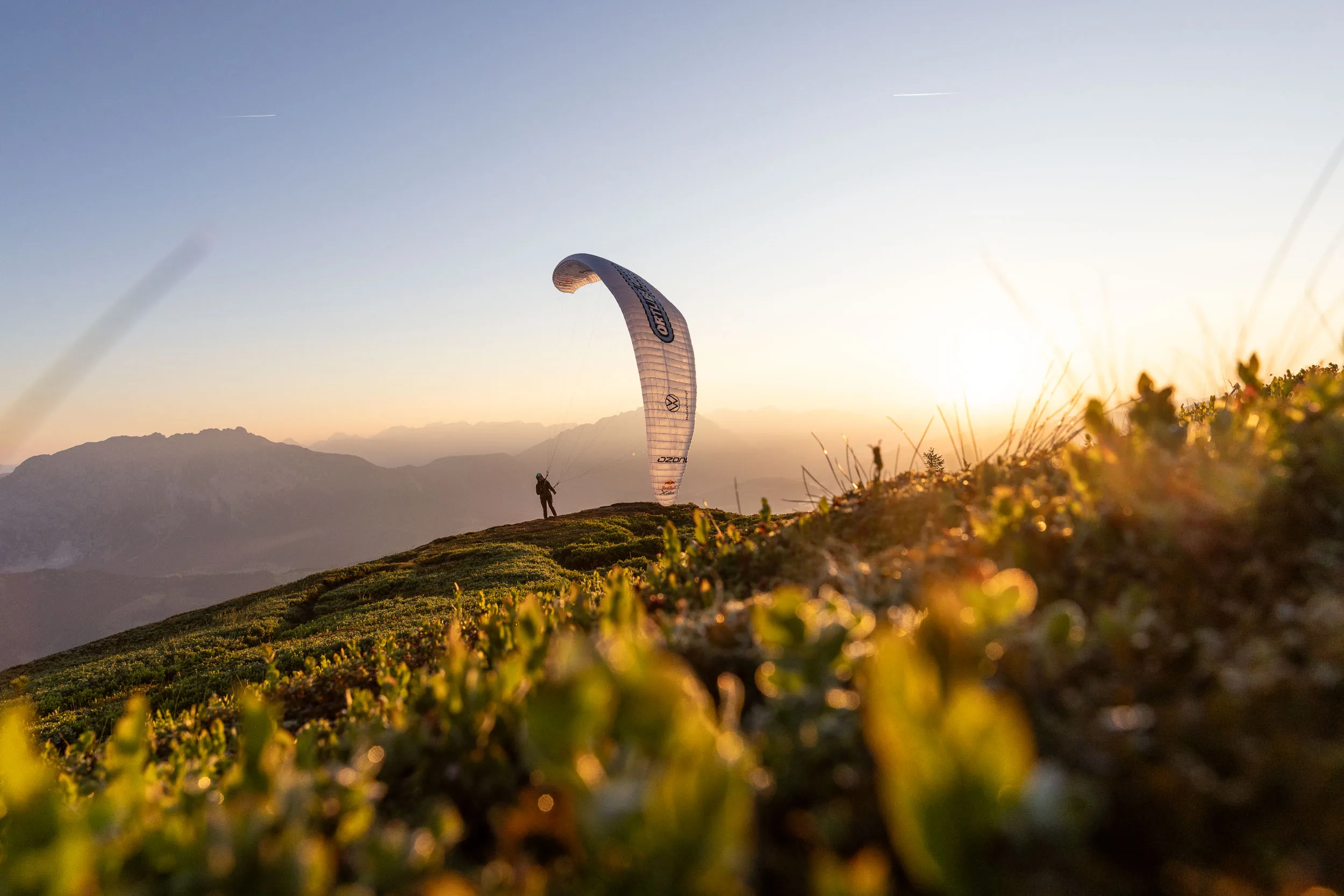 Gleitschirm ueber einem sonnigen Bergruecken im Ennstal