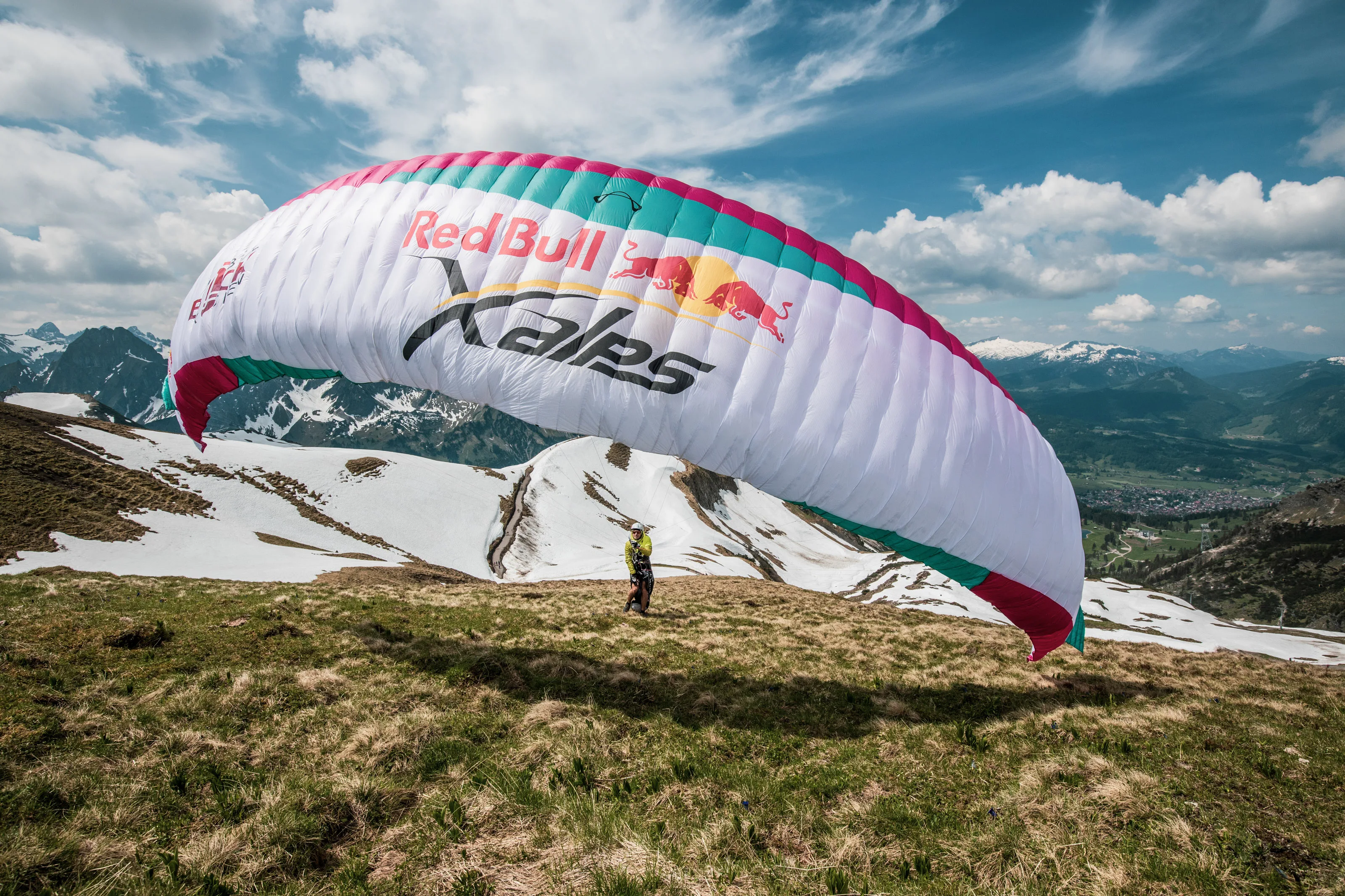 Michael Lacher steht unter dem weit aufgezogenen pinkweißen Gleitschirm auf einer Bergwiese.