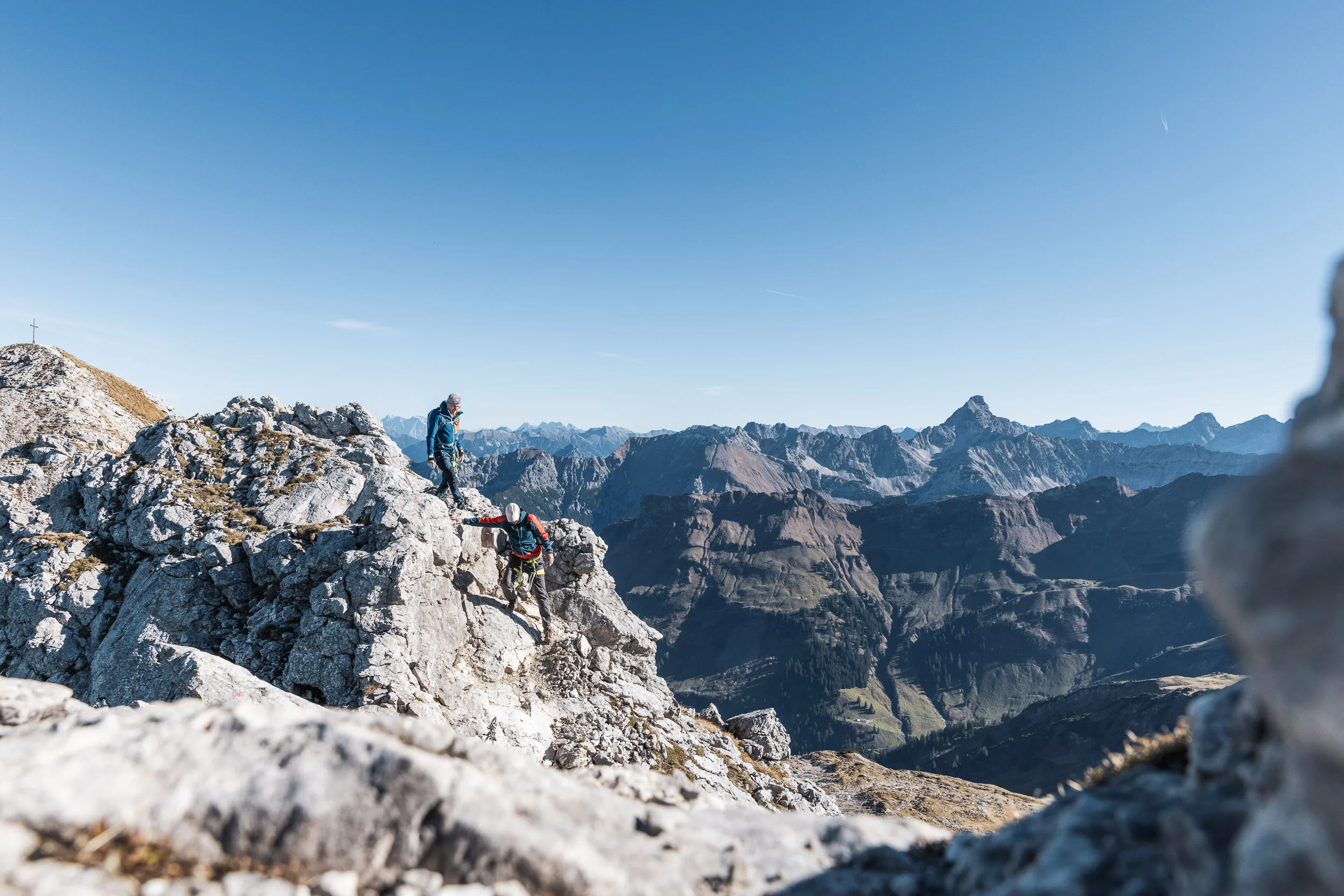 Zwei Bergsteiger queren einen felsigen Grat vor dem weiten Panorama der Allgäuer Alpen.