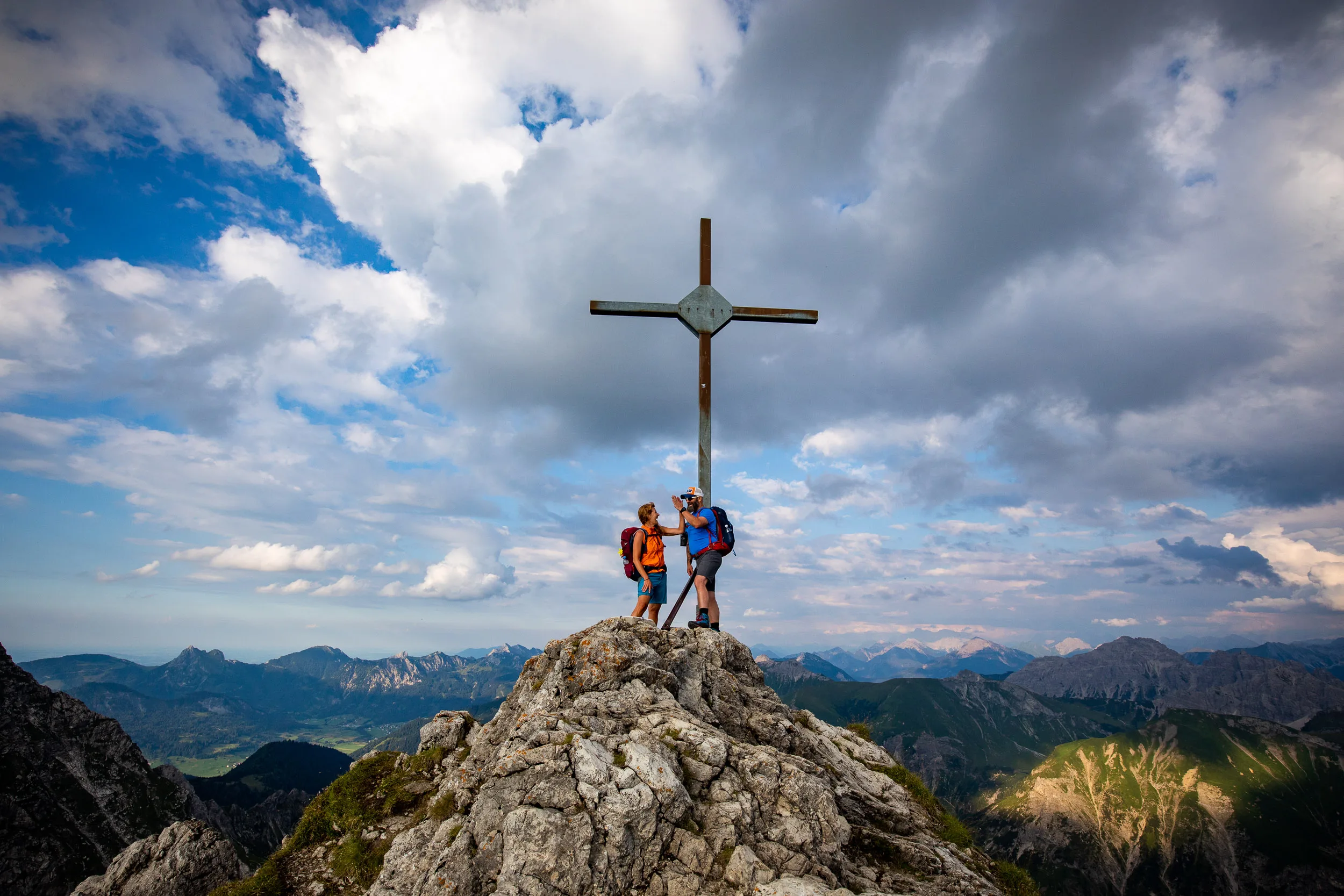 Caroline Nantke und Harald Dreyer stehen am Gipfelkreuz vor einem weiten Bergpanorama