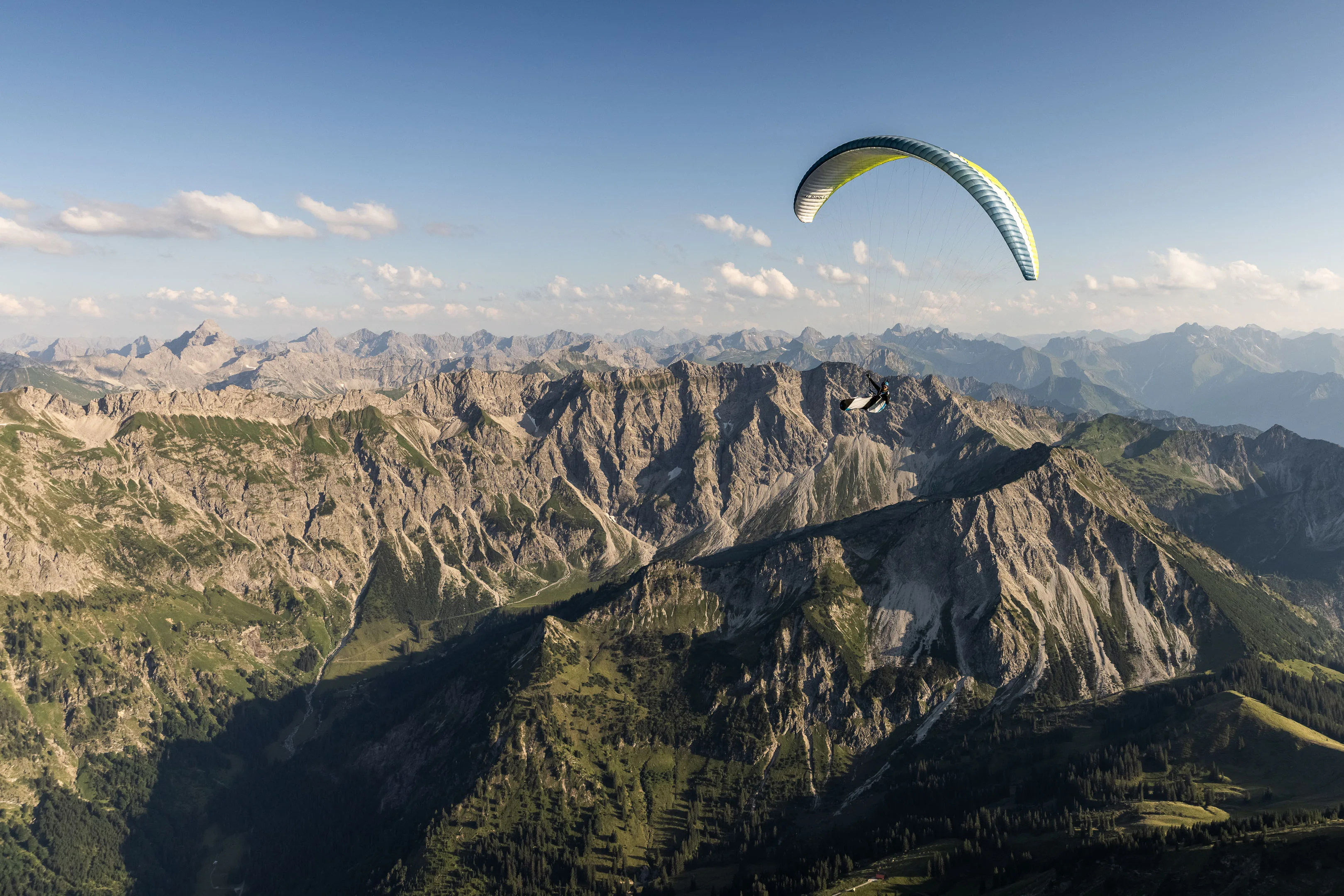 Ein Gleitschirm zieht über einen schroffen Bergrücken mit weitem Alpenpanorama