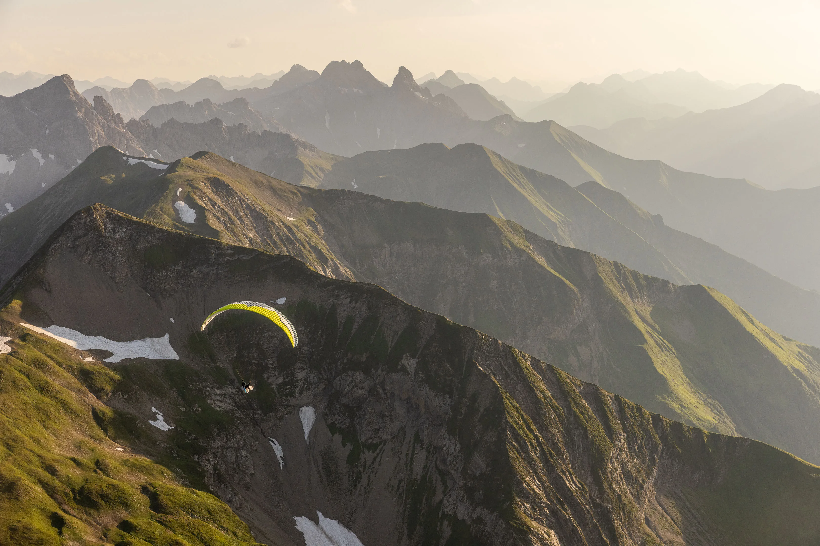 Ein Gleitschirm fliegt unterhalb eines Grats über einer steilen Felsflanke