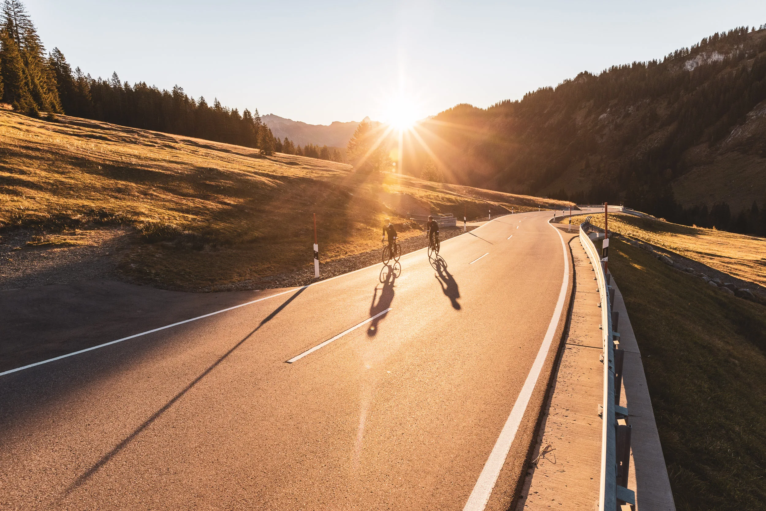 Zwei Rennradfahrerinnen folgen der Straße in eine sonnige Kurve