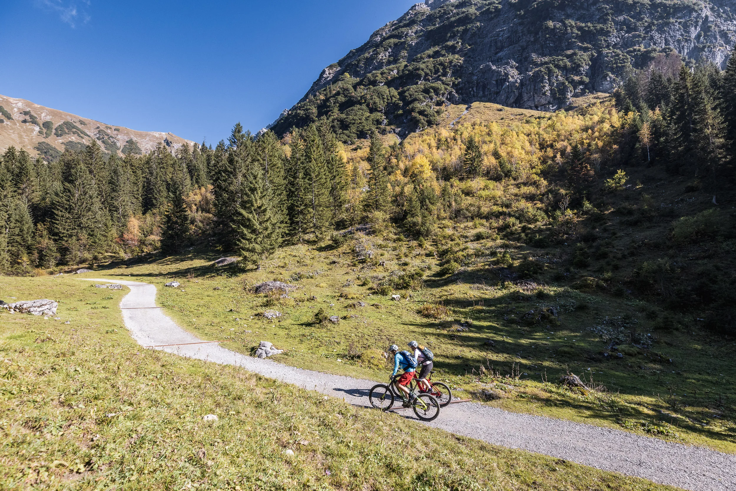 Silvi Vogel und Andrea Geiger fahren mit Mountainbikes auf einem Bergweg unter Felsen