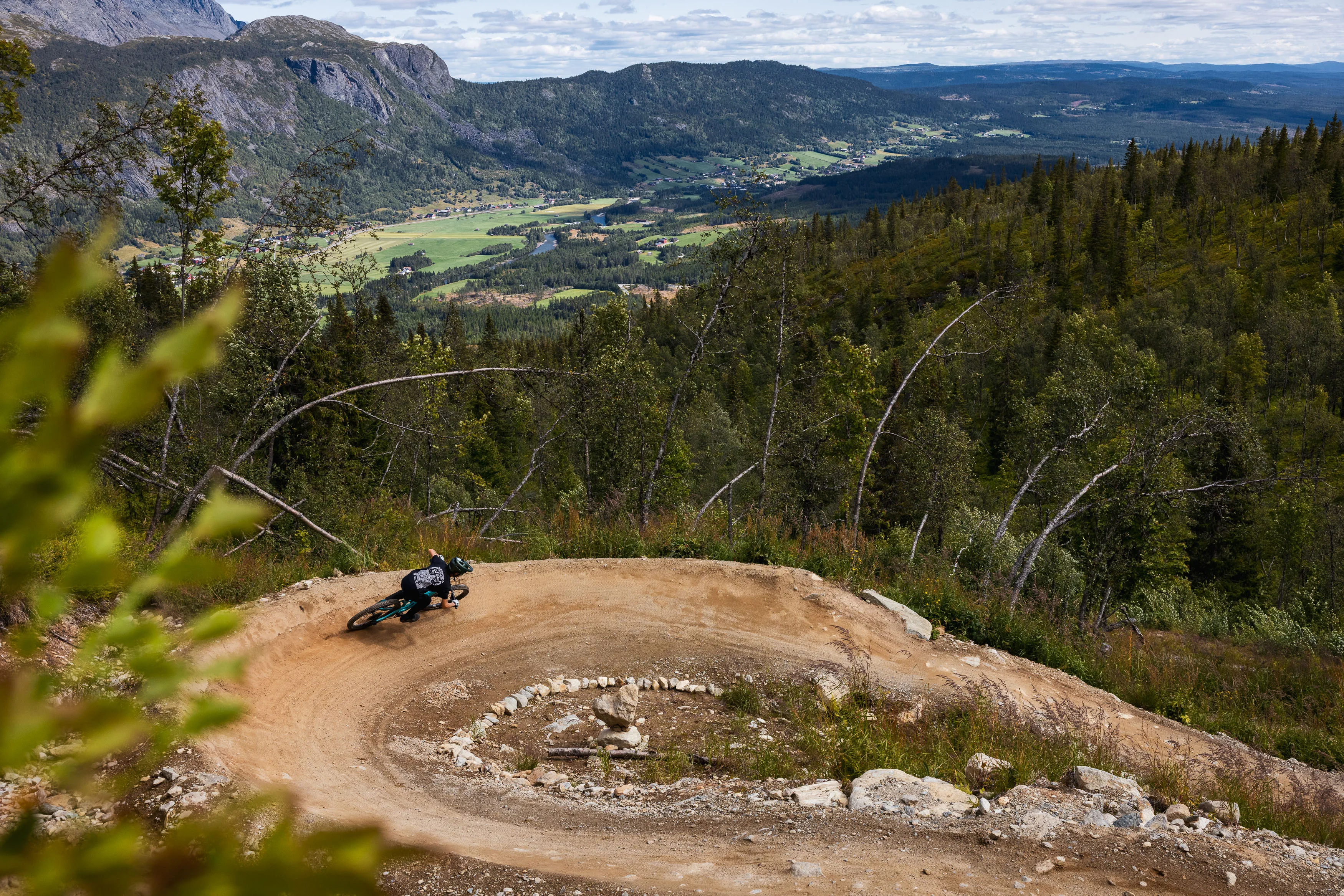 Mountainbiker fährt in tiefer Schräglage durch einen staubigen Anlieger über dem Tal