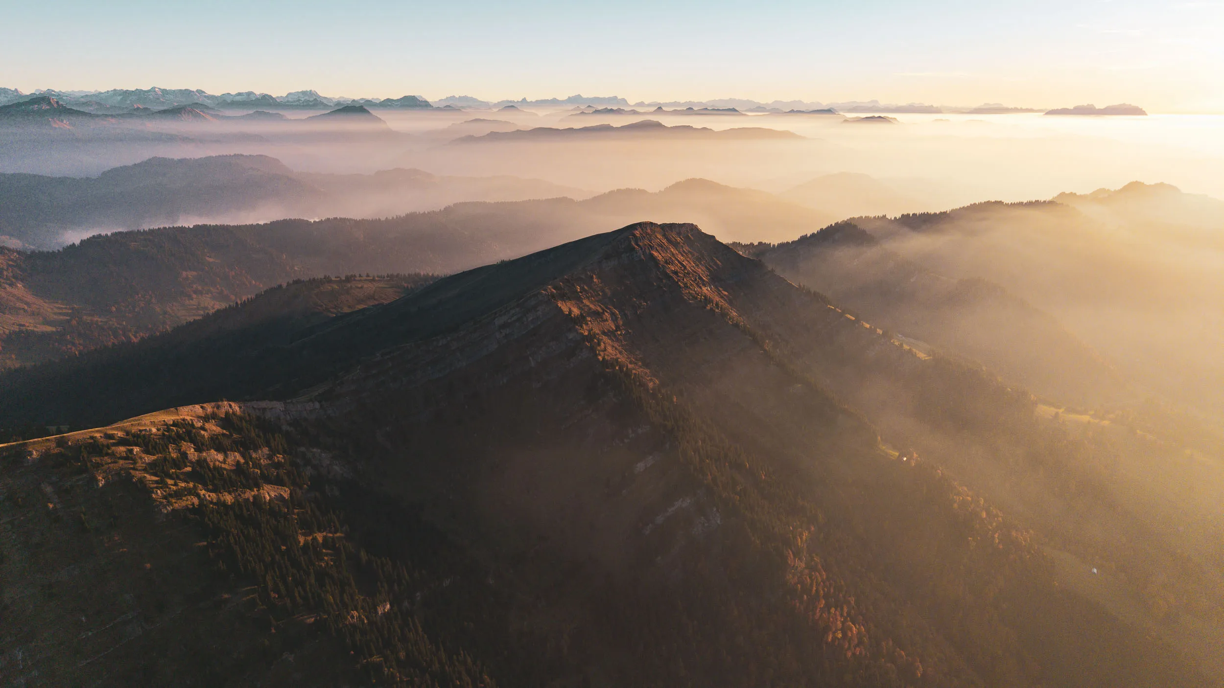 Tiefe Sonnenstrahlen brechen über einen dunklen Bergkamm und dunstige Täler