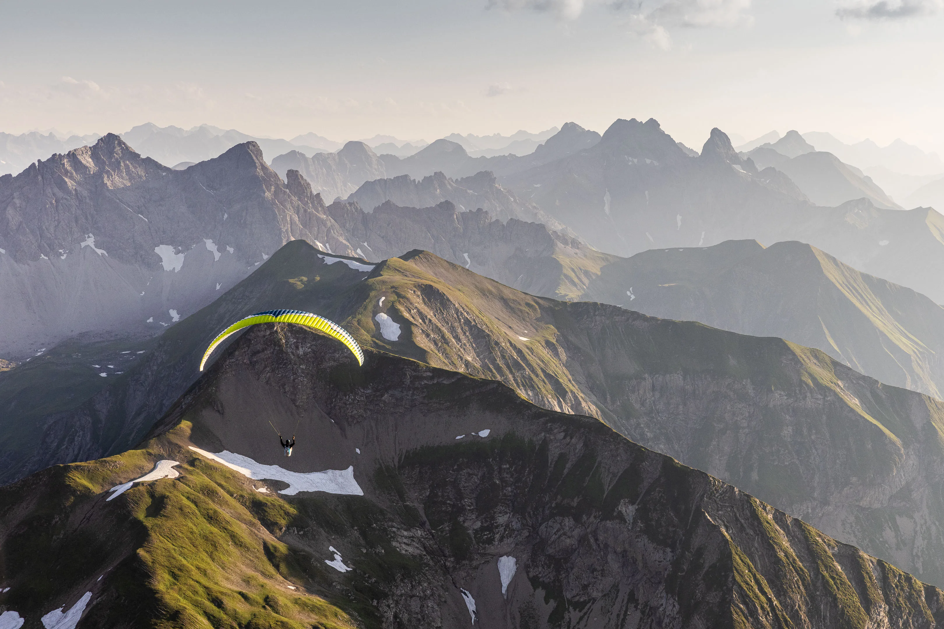 Ein Gleitschirm kommt über einem dunklen Bergkessel vor hellem Horizont entgegen