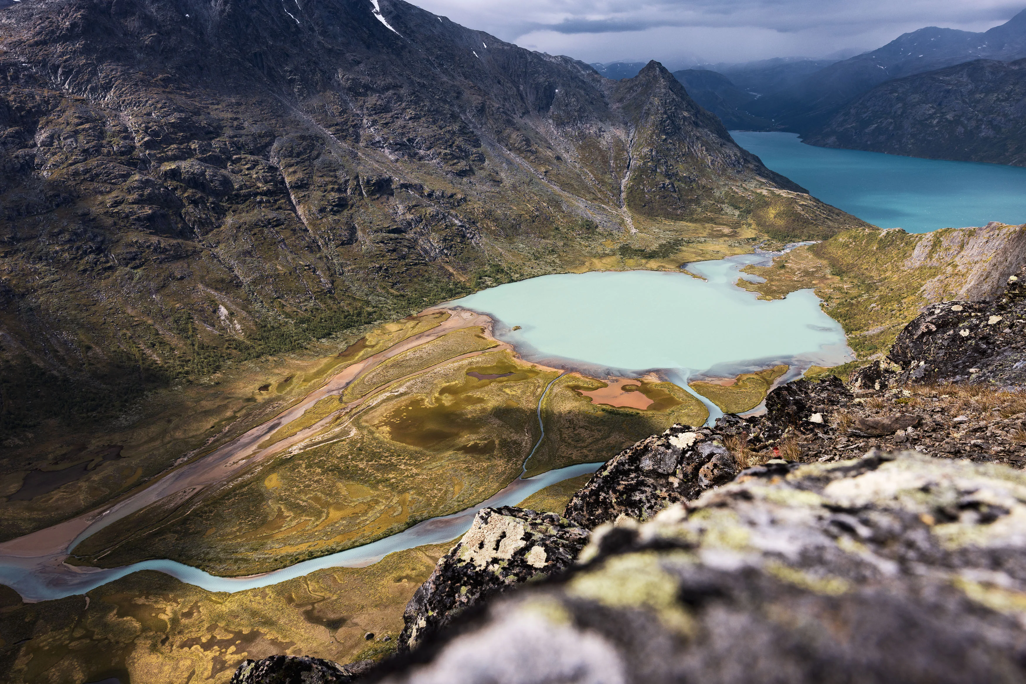 Blick über Felsen auf einen hellen Bergsee und ein verzweigtes Flussdelta