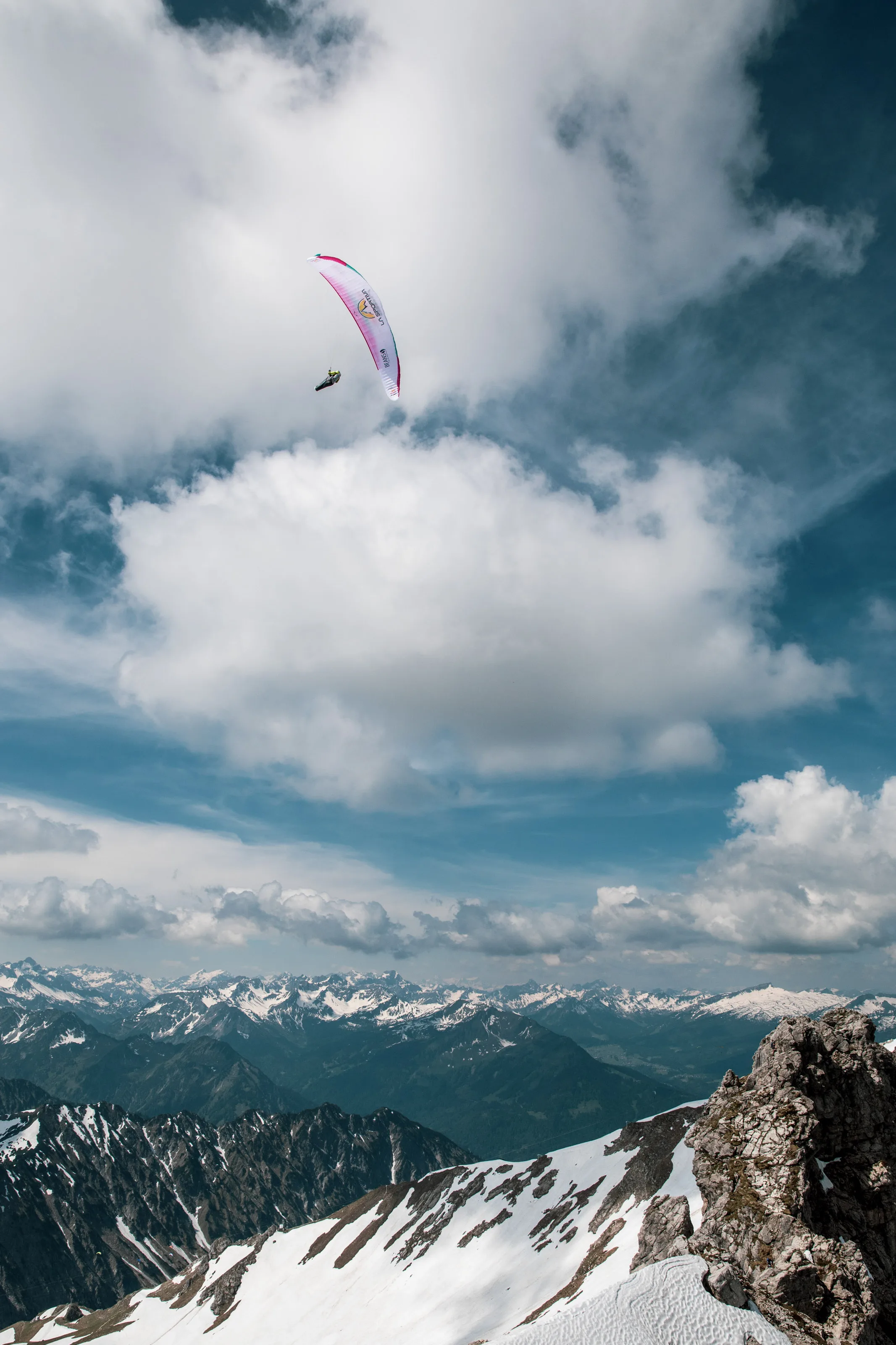 Der Gleitschirm von Michael Lacher schwebt zwischen Wolken über einem felsigen Gipfel.
