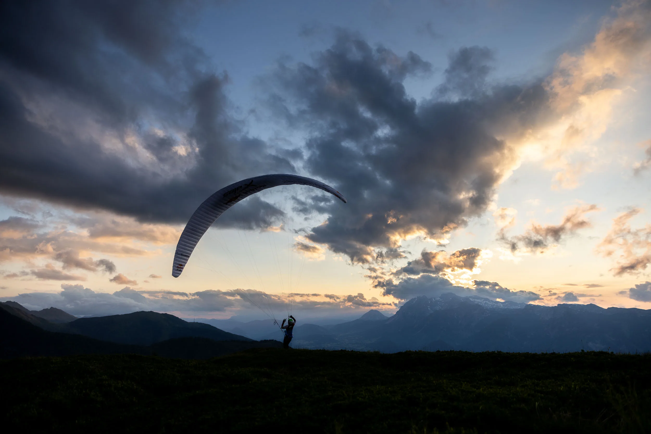 Gleitschirmpilotin startet vor dunklen Wolken ueber dem Ennstal