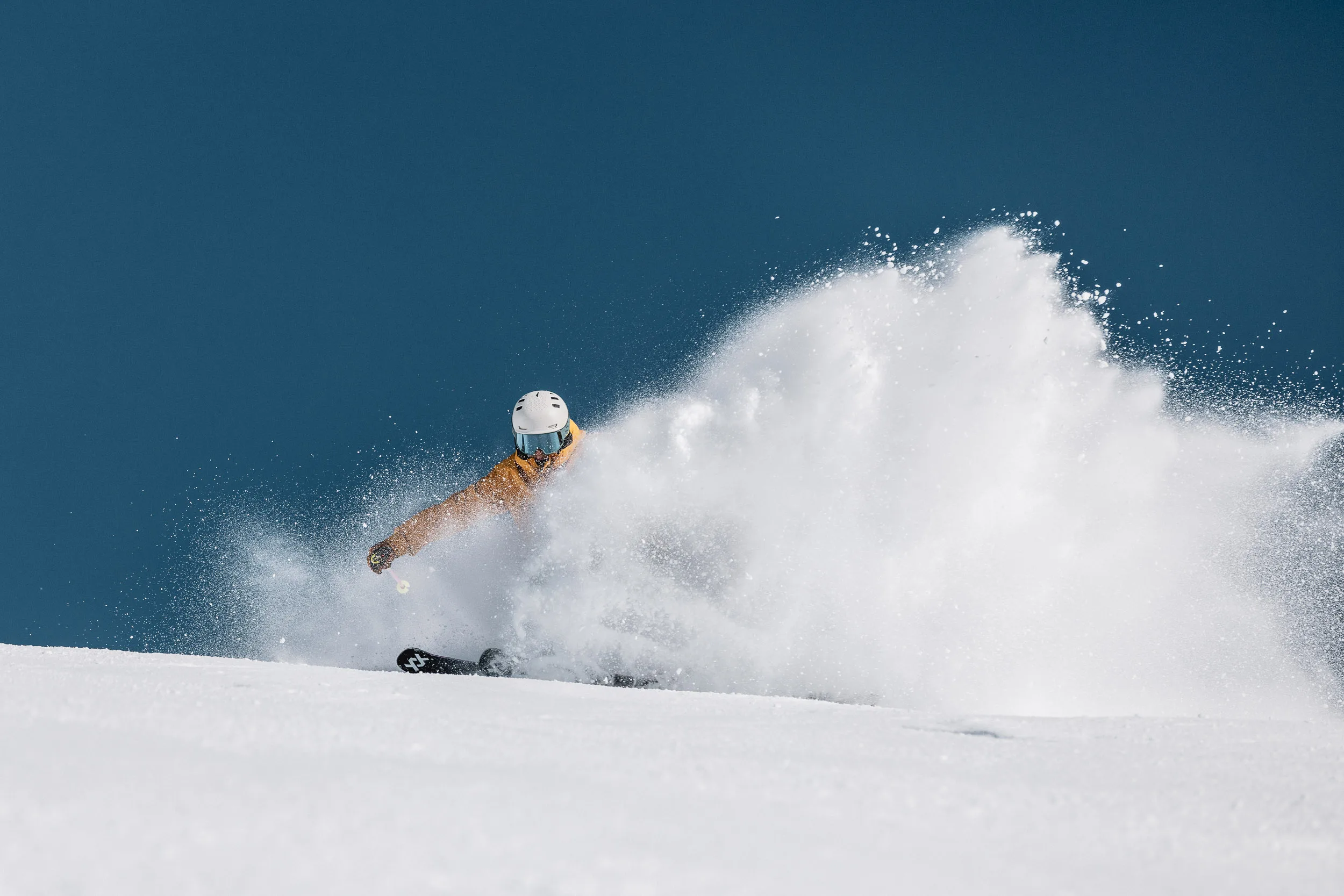Skilehrer fährt durch eine hohe Wolke aus aufspritzendem Schnee