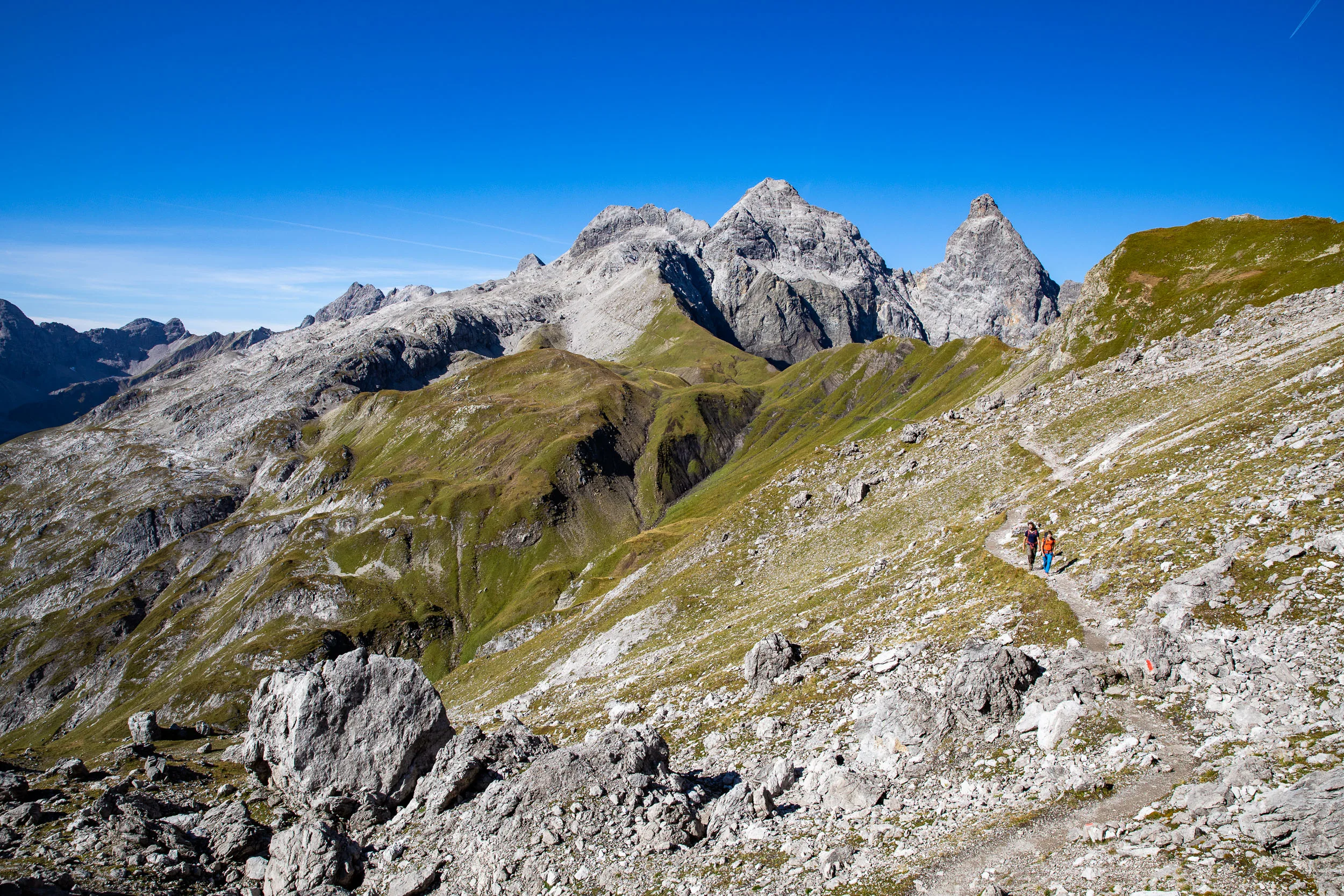 Raphaela Haug und Tom Besser wandern durch eine grüne Mulde vor hellen Felsgipfeln