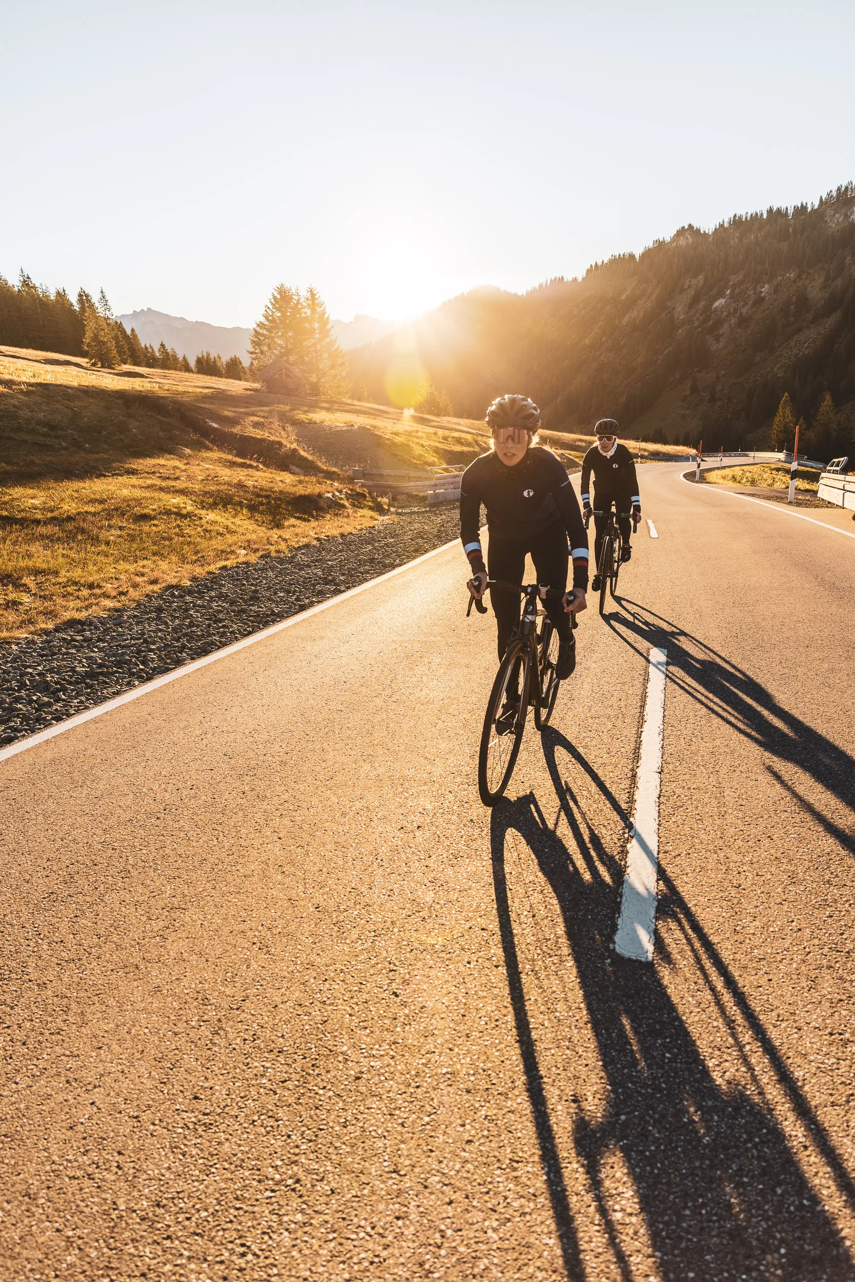 Zwei Rennradfahrerinnen auf der Passstraße mit langen Schatten im Abendlicht