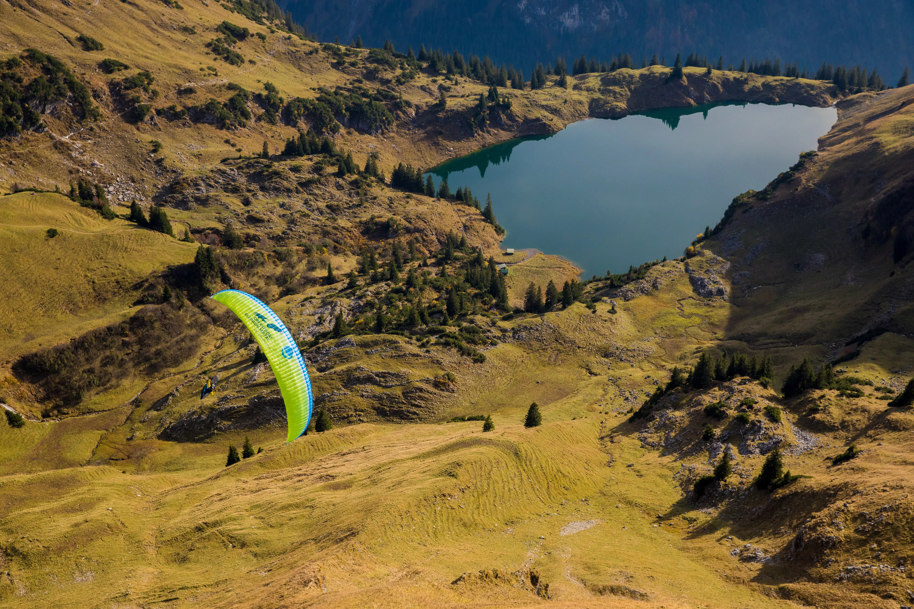 Michael Gebert unter einem grünen Gleitschirm über dem Seealpsee inmitten herbstlicher Alpenlandschaft