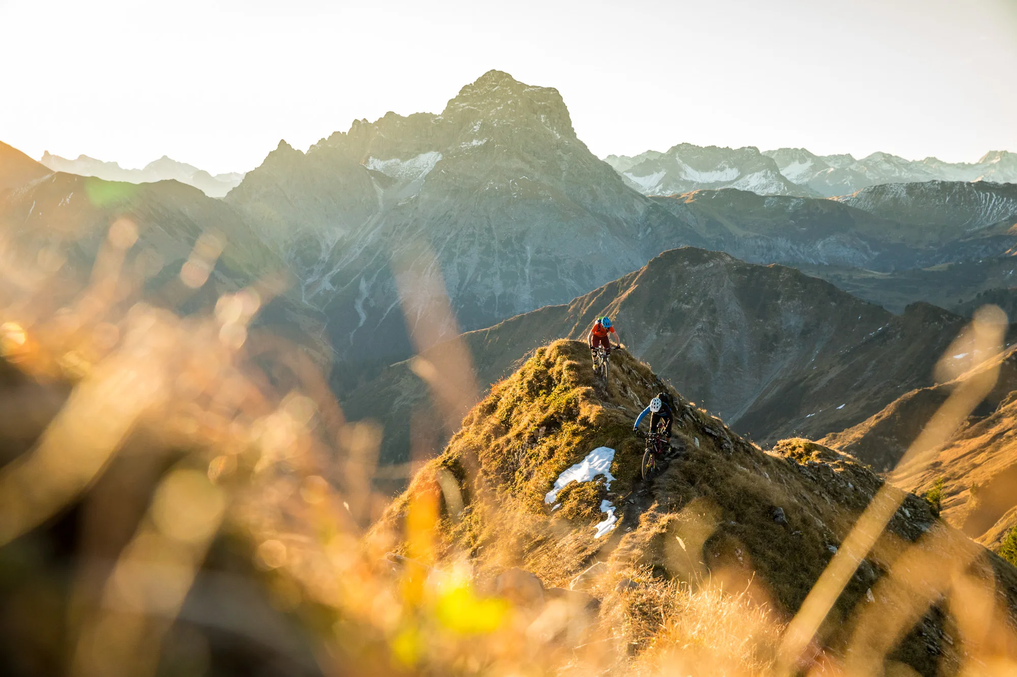 Mountainbiker auf einer grasigen Bergkante mit Gipfeln und Tal im Hintergrund