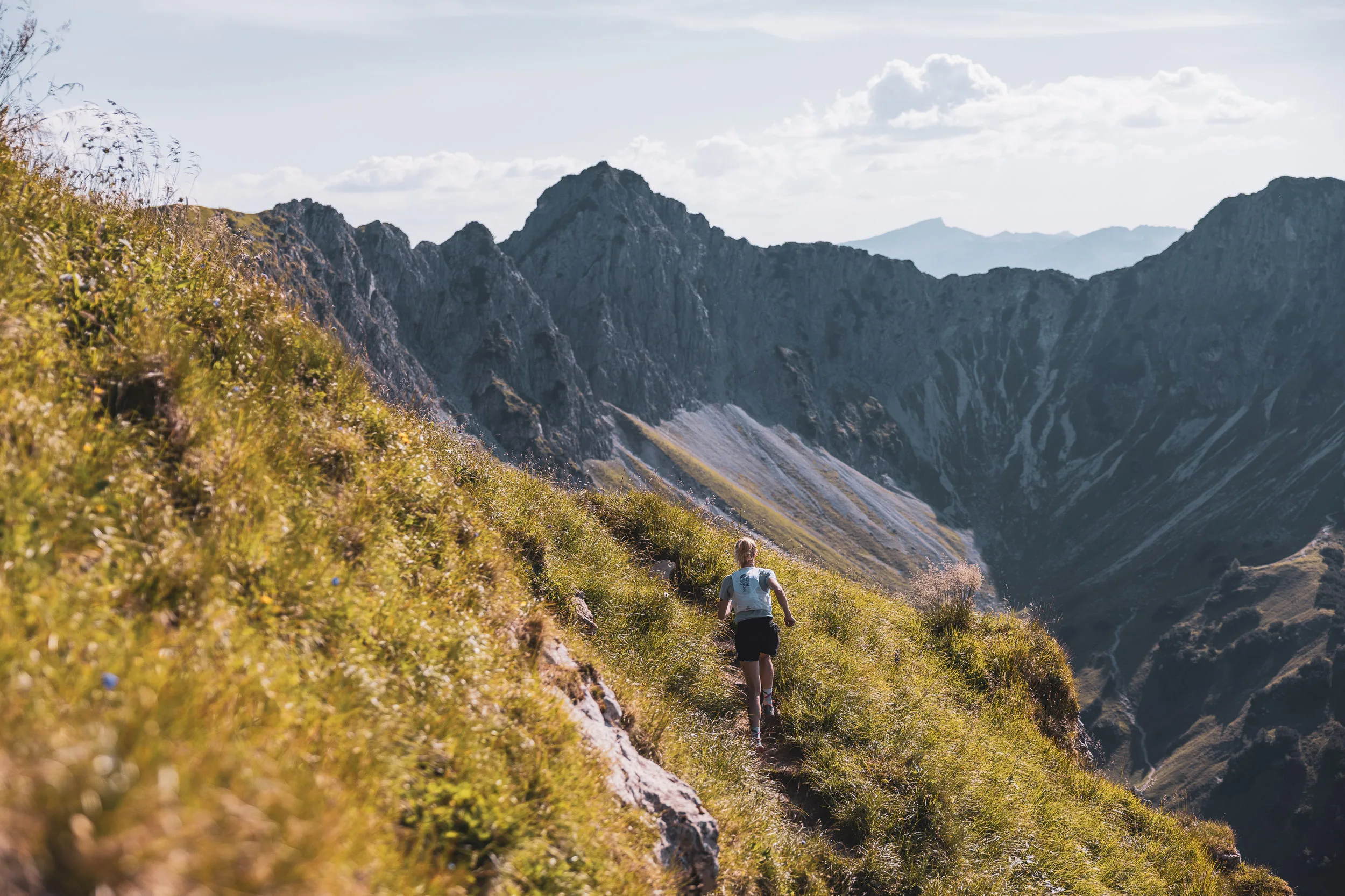 Trailrunnerin auf einem schmalen Grasgrat vor einer dunklen Bergkette