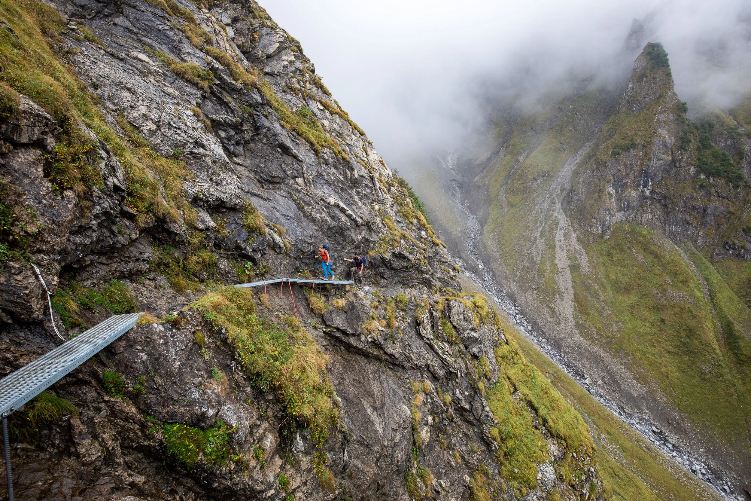 Raphaela Haug und Tom Besser queren einen schmalen Weg über einem tiefen Bergtal