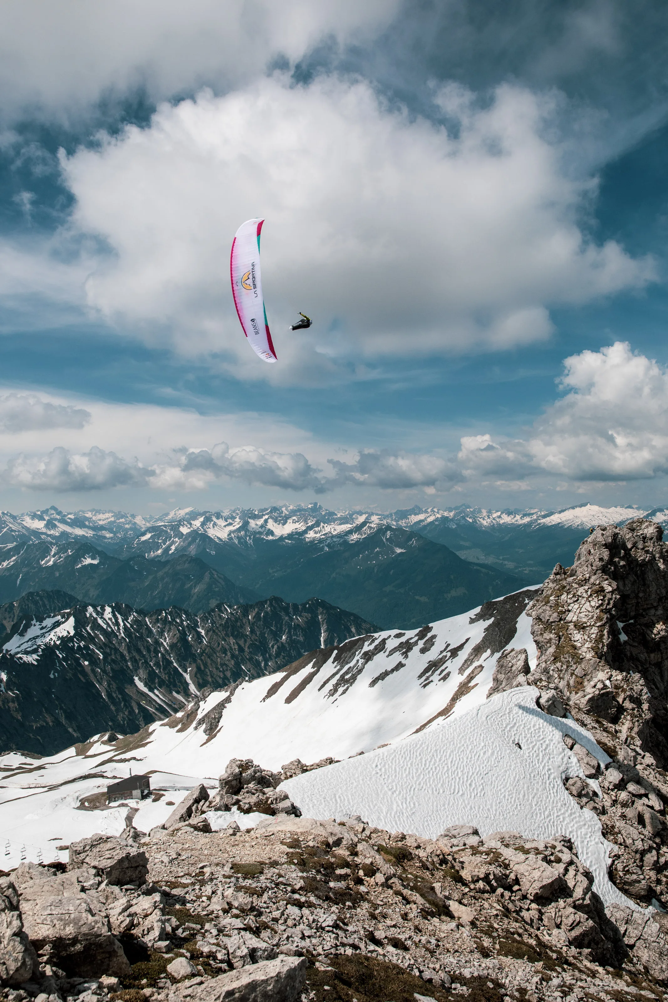 Michael Lacher fliegt mit Gleitschirm über einem verschneiten Grat vor der fernen Alpenkette.