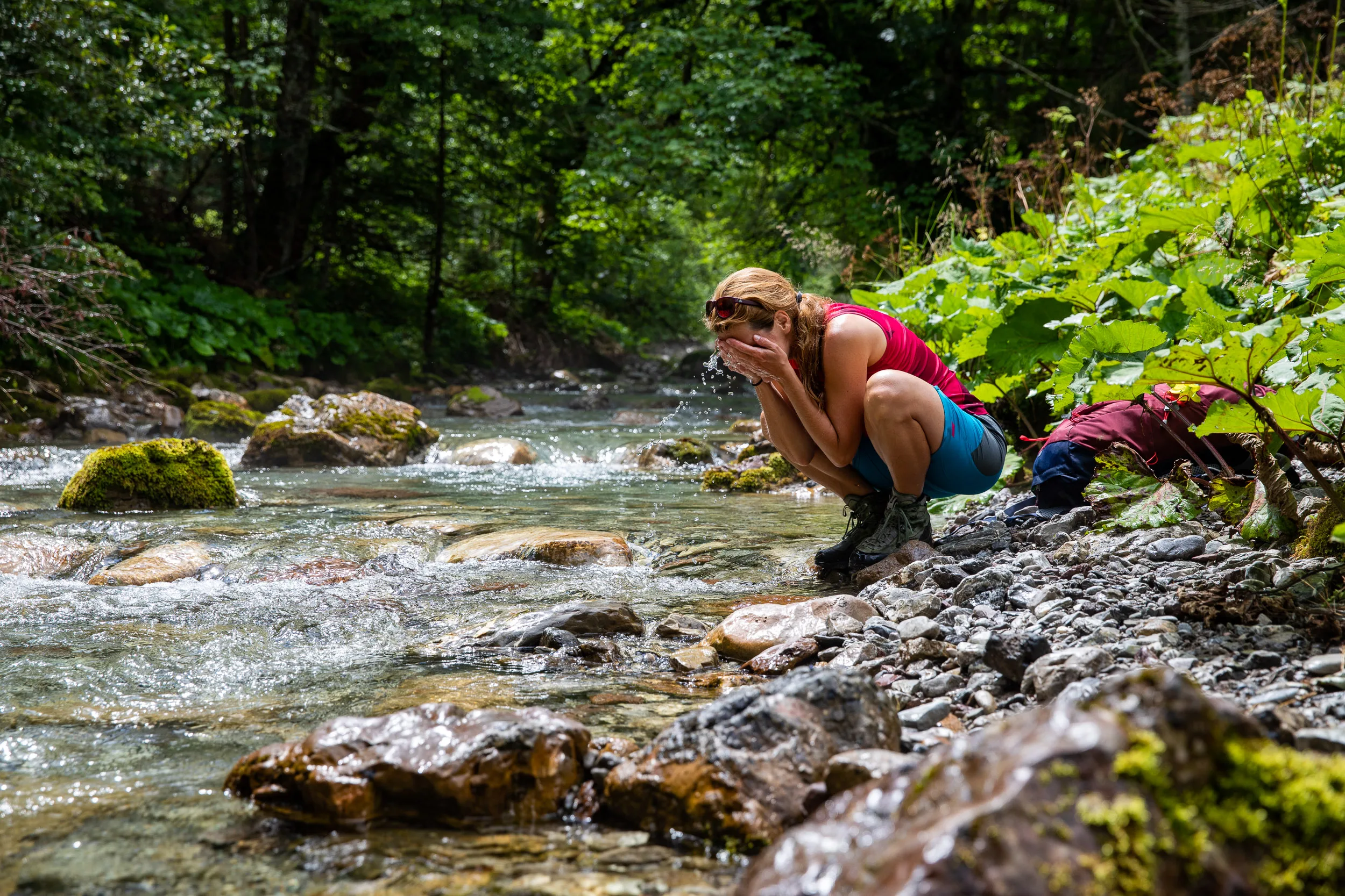 Caroline Nantke schöpft Wasser aus einem Bach zwischen moosigen Steinen