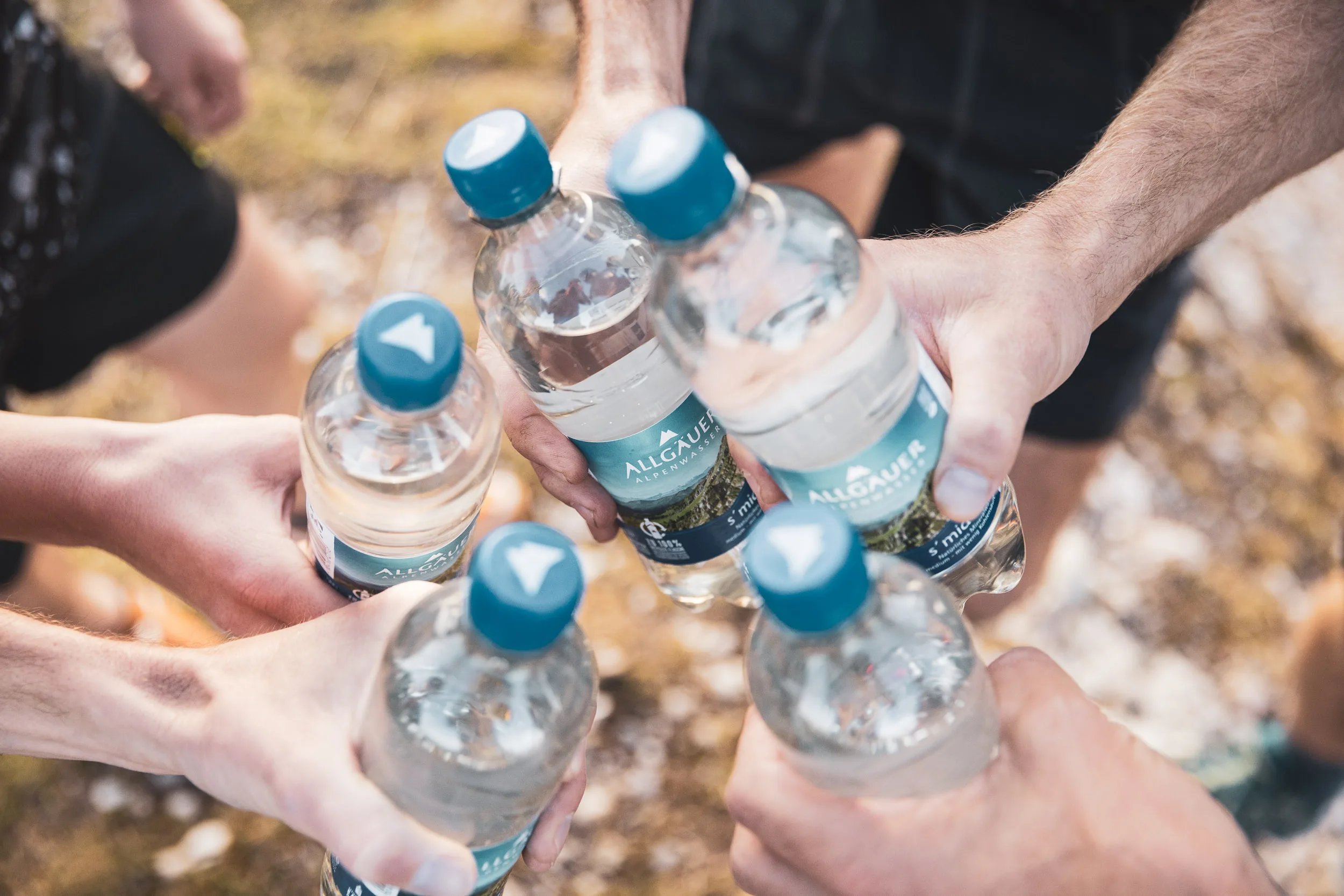 Mehrere Haende halten Mineralwasserflaschen an einer Bergquelle zusammen