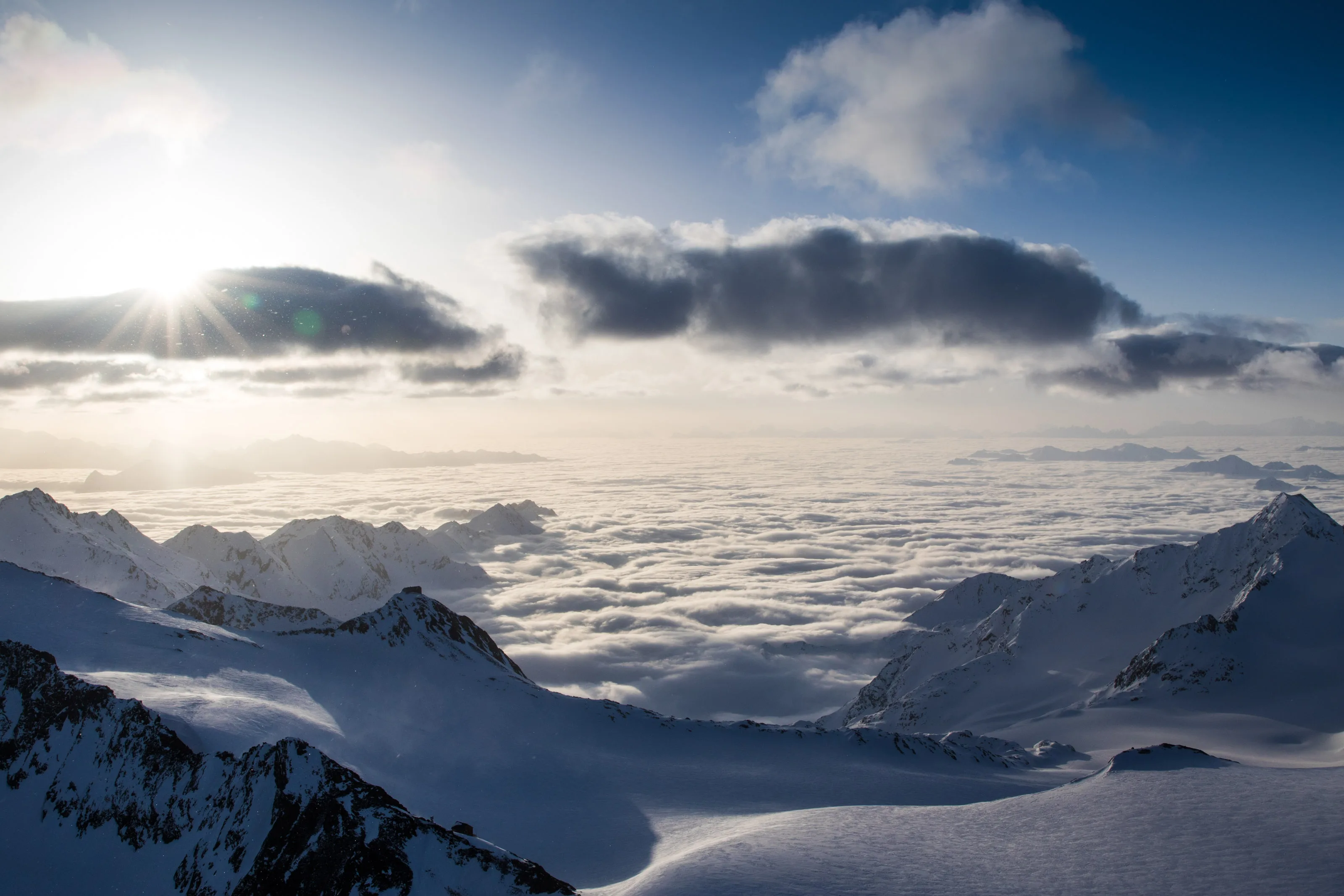 Tief stehende Sonne beleuchtet die winterlichen Hochalpen über einer geschlossenen Wolkendecke